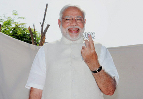 BJP PM candidate and Gujarat Chief Minister Narendra Modi shows his inked finger along with a cut-out of party symbol 'lotus' during a press conference after casting his vote at a polling station in Ahmedabad on Wednesday. PTI Photo