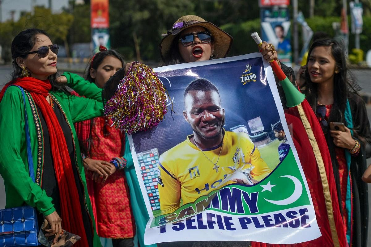 Spectators carry a poster featuring an image of Peshawar Zalmi's team captain Darren Sammy outside the National Cricket Stadium in Karachi on February 21, 2020, ahead of the start of the Pakistan Super League (PSL) T20 cricket match between Peshawar Zalmi