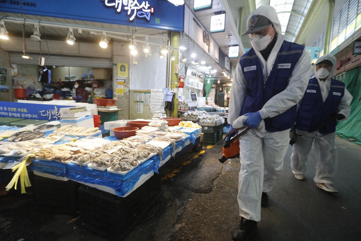 Workers wearing protective gears spray disinfectant as a precaution against the coronavirus at a market in Seoul. AP/PTI