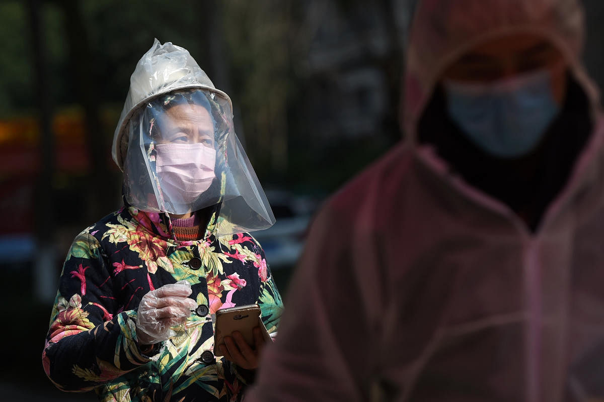 Resident wearing makeshift protective face shield waits to collect food and necessities purchased through group orders at an entrance to a residential compound in Wuhan. Credit: Reuters Photo