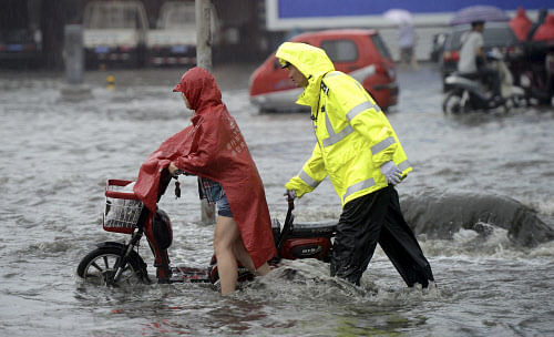A policeman helps a resident to push an electric bicycle at a flooded street during a heavy rain in Jinan, Shandong province, July 23, 2013. REUTERS