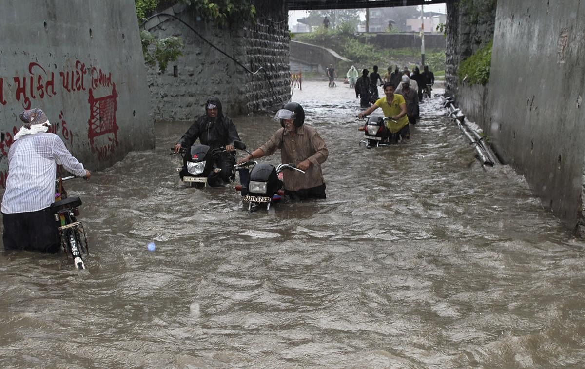 Commuters wade through a waterlogged street after heavy rainfall in Surat on Thursday. PTI