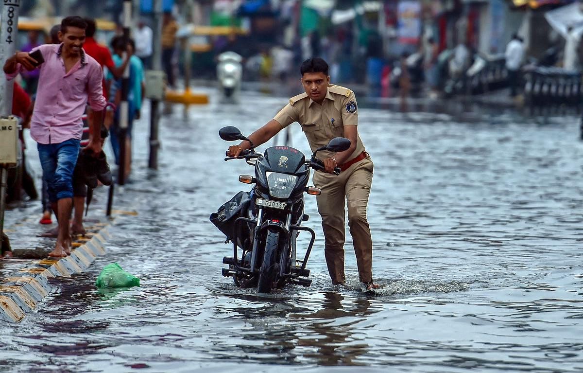 A police personal wades through a waterlogged street after heavy rainfall at Maninagar, in Ahmedabad on Friday. PTI