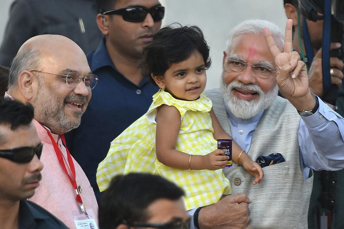 Prime Minister Narendra Modi flashes the victory sign as he holds the granddaughter (C) of BJP president Amit Shah (L) after arriving to cast his vote during the third phase of general elections at a polling station in Ahmedabad on April 23, 2019. (AFP Photo)