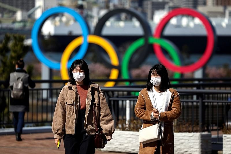People wearing protective face masks, following an outbreak of the coronavirus, are seen in front of the Giant Olympic rings at the waterfront area at Odaiba Marine Park in Tokyo. (Reuters Photo)