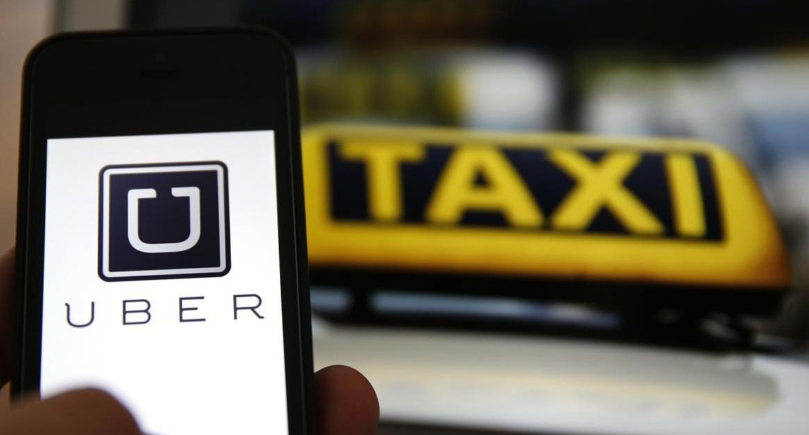 An illustration picture shows the logo of car-sharing service app Uber on a smartphone next to the picture of an official German taxi sign (Credit:  REUTERS/Kai Pfaffenbach)