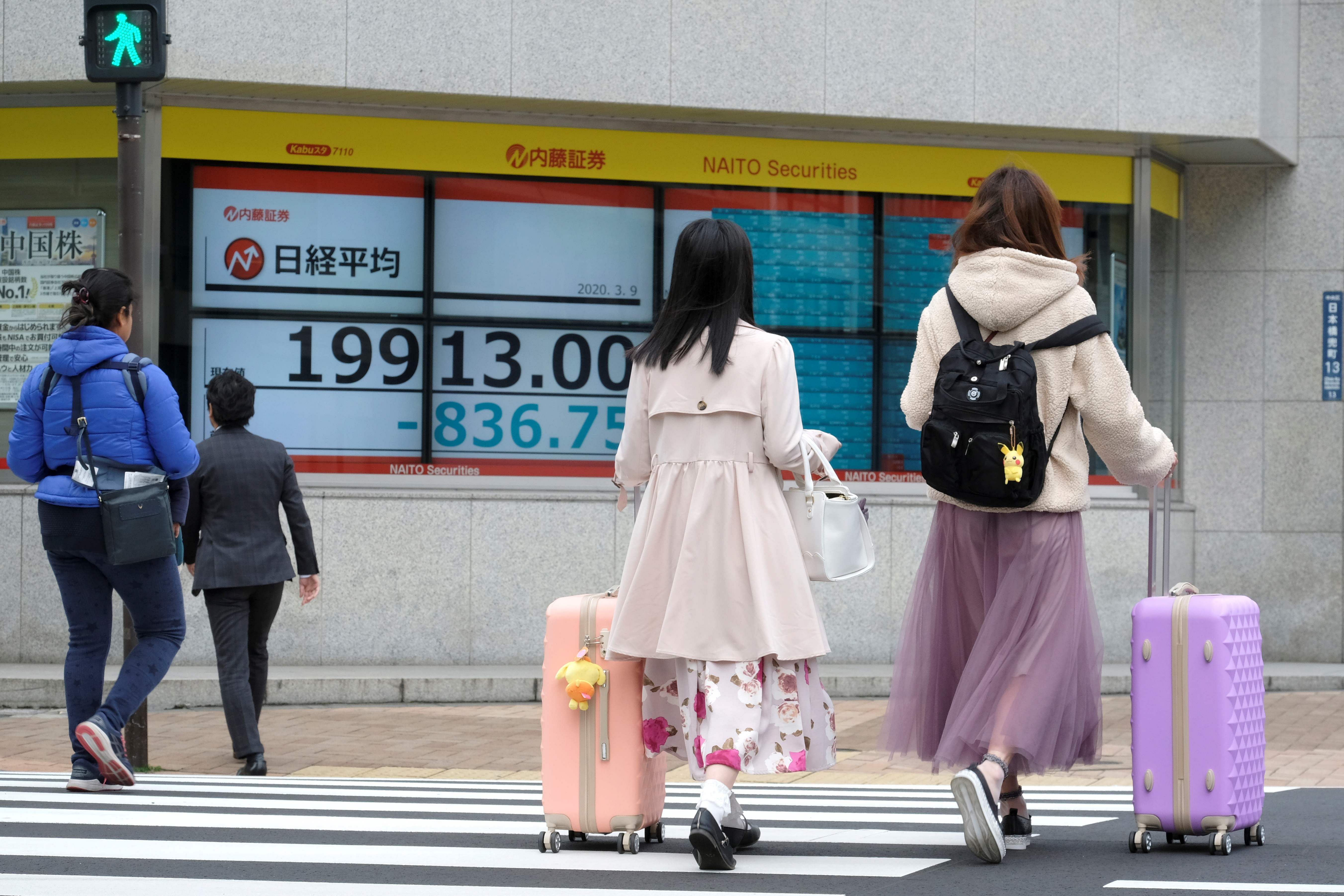 Pedestrians walk in front of a quotation board displaying the share price numbers of the Tokyo Stock Exchange in Tokyo. (Credit: AFP)
