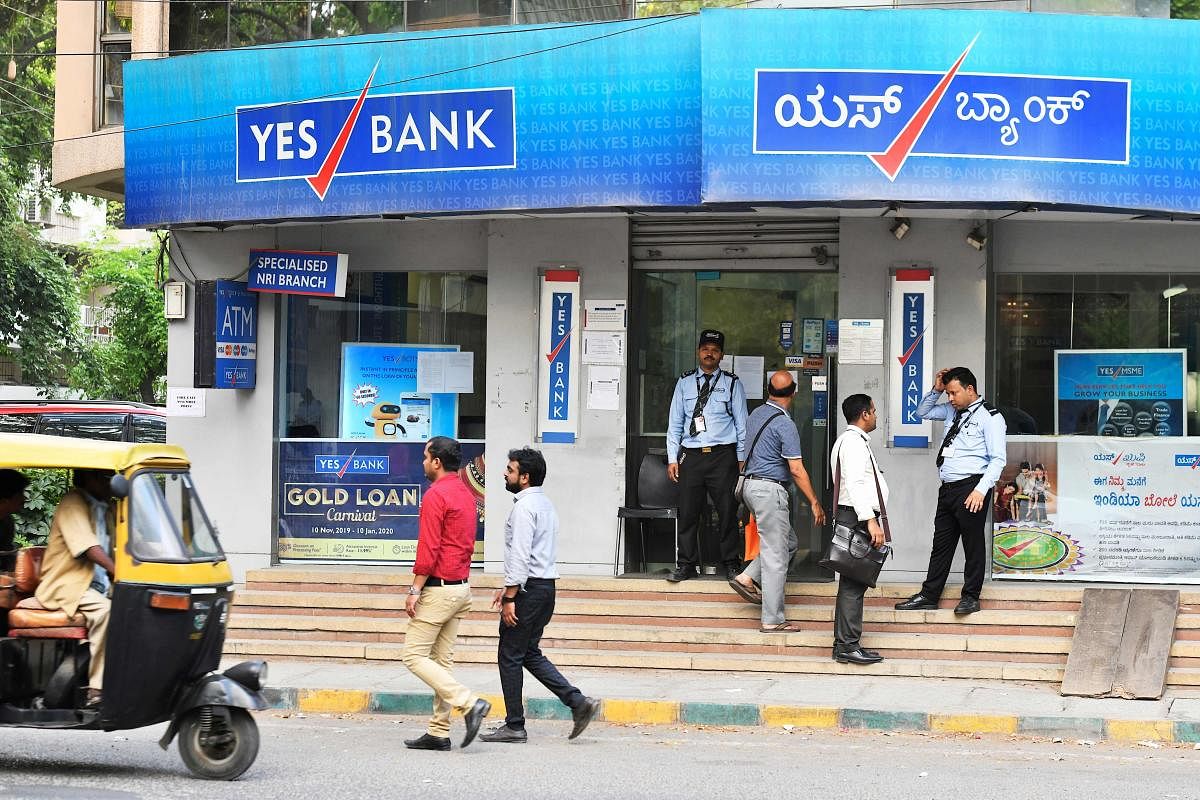 Customers make enquiries with the security personnel at a Yes Bank branch in Bangalore on March 6, 2020. (AFP Photo)