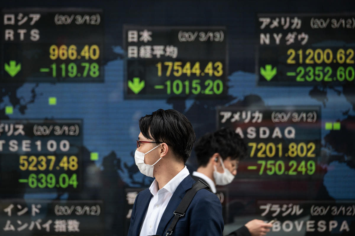 Pedestrians wearing face masks walk past an electric board showing the Nikkei 225 index (C) on the Tokyo Stock Exchange in Tokyo. AFP