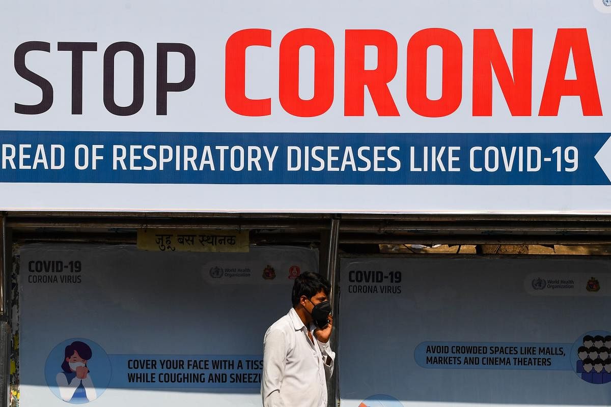 A man uses his mobile phone standing in front of an awareness board displaying preventive measures against the COVID-19 coronavirus at a bus stop in Mumbai. AFP