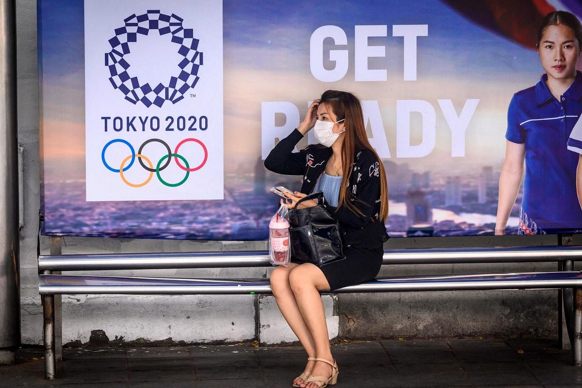 A woman wearing a facemask, amid concerns over the spread of the COVID-19 coronavirus, sits at a bus stop in front of a Tokyo 2020 Olympics advertisement (AFP Photo)