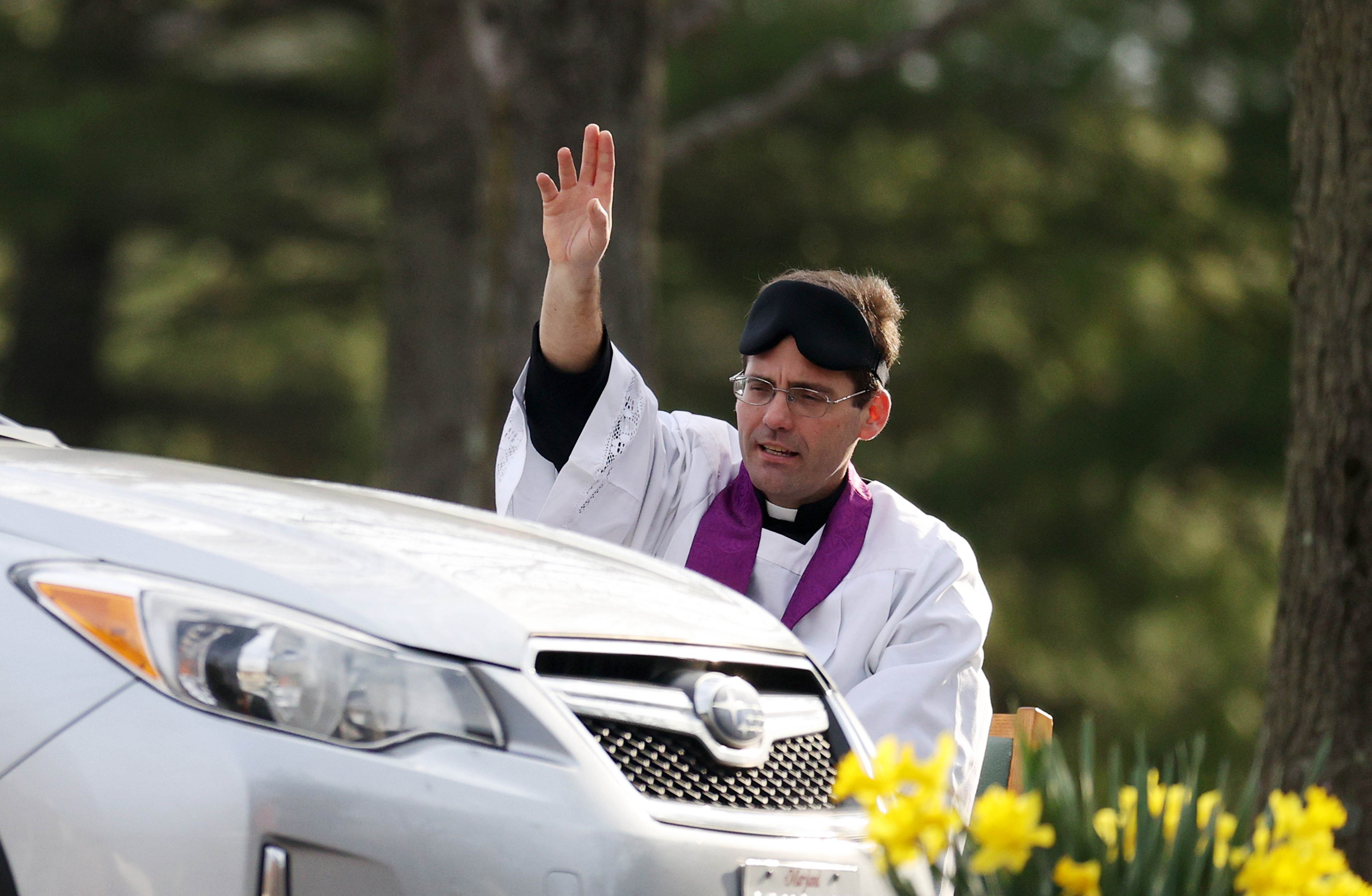 The Rev. Scott Holmer of St. Edward the Confessor Catholic Church makes the sign of the cross after holding confession in the church parking lot on March 20, 2020 in Bowie, Maryland. Holmer, who sits six feet away from those in cars, holds drive thru confessions daily in the parking lot of the church due to the outbreak of the COVID-19 pandemic. (Credit: AFP)