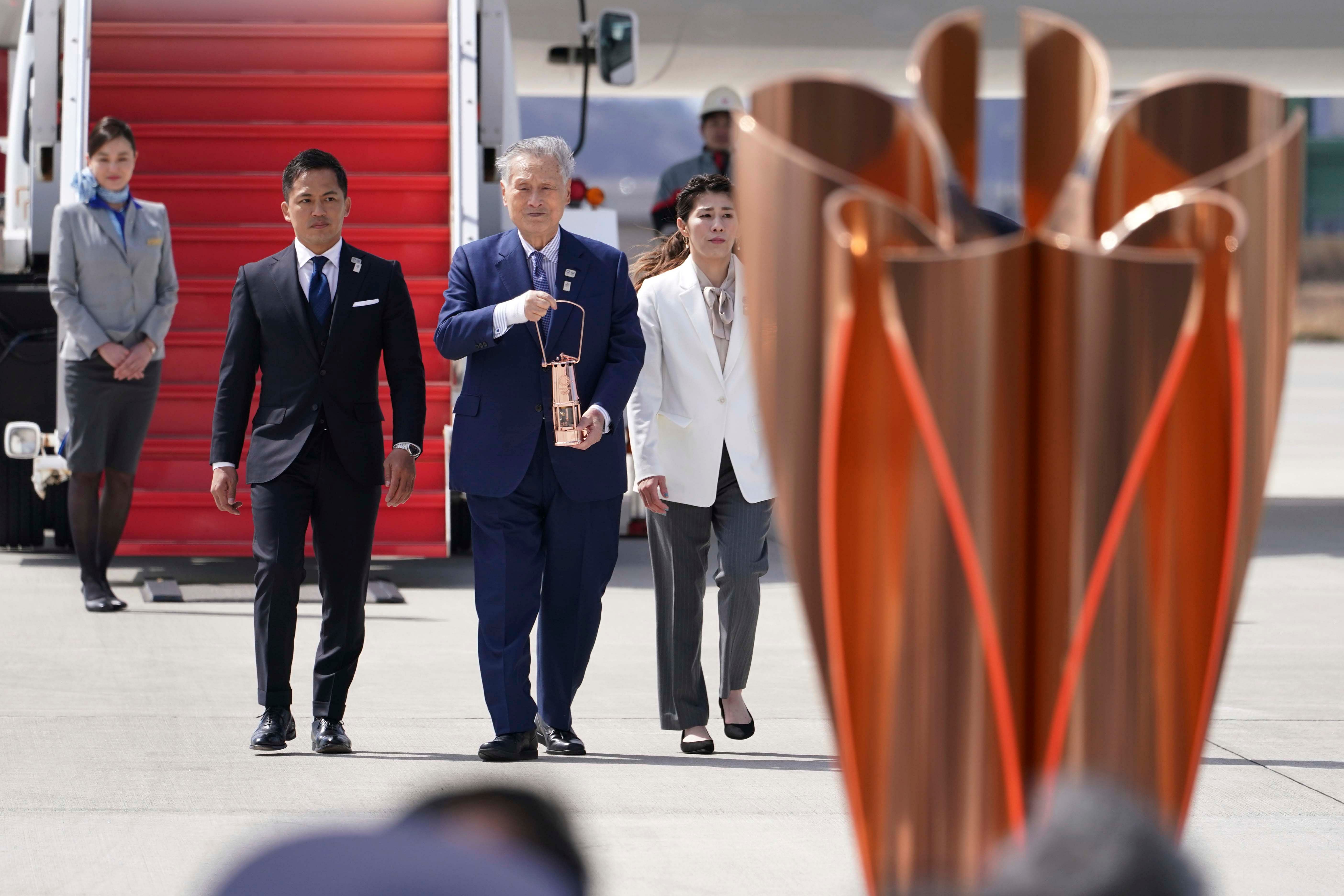 Tokyo 2020 Olympics chief Yoshiro Mori, center, followed by three-time Olympic gold medalists Tadahiro Nomura and Saori Yoshida, right, carries the Olympic flame during the Flame Arrival Ceremony at Japan Air Self-Defense Force Matsushima Base in Higashimatsushima in Miyagi Prefecture, north of Tokyo. (Credit: AFP)