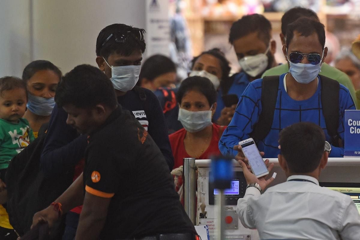 Passengers wearing facemasks amid concerns over the spread of the COVID-19 novel coronavirus, stand in a queue at a counter inside the airport in Goa. (AFP Photo)