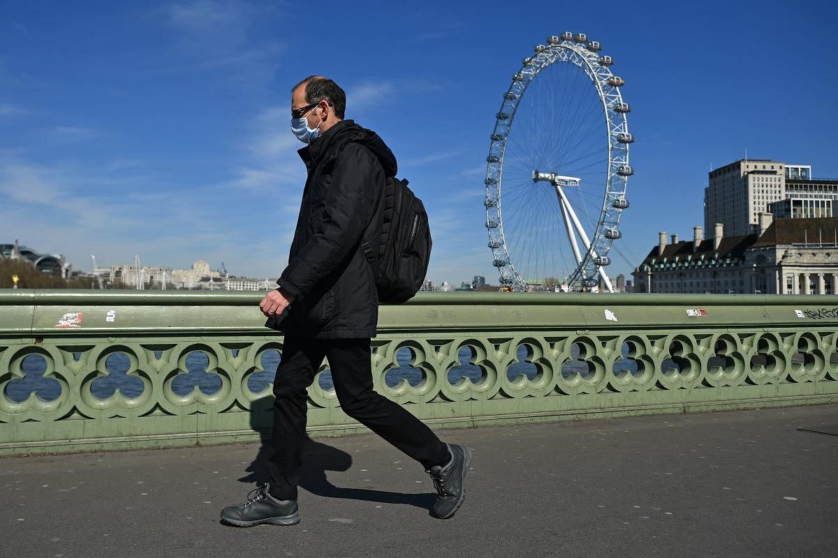 A man wearing a protective face mask walks over a deserted Westminster Bridge with the London Eye seen behind, in central London, March 23, 2020, Credit: AFP Photo