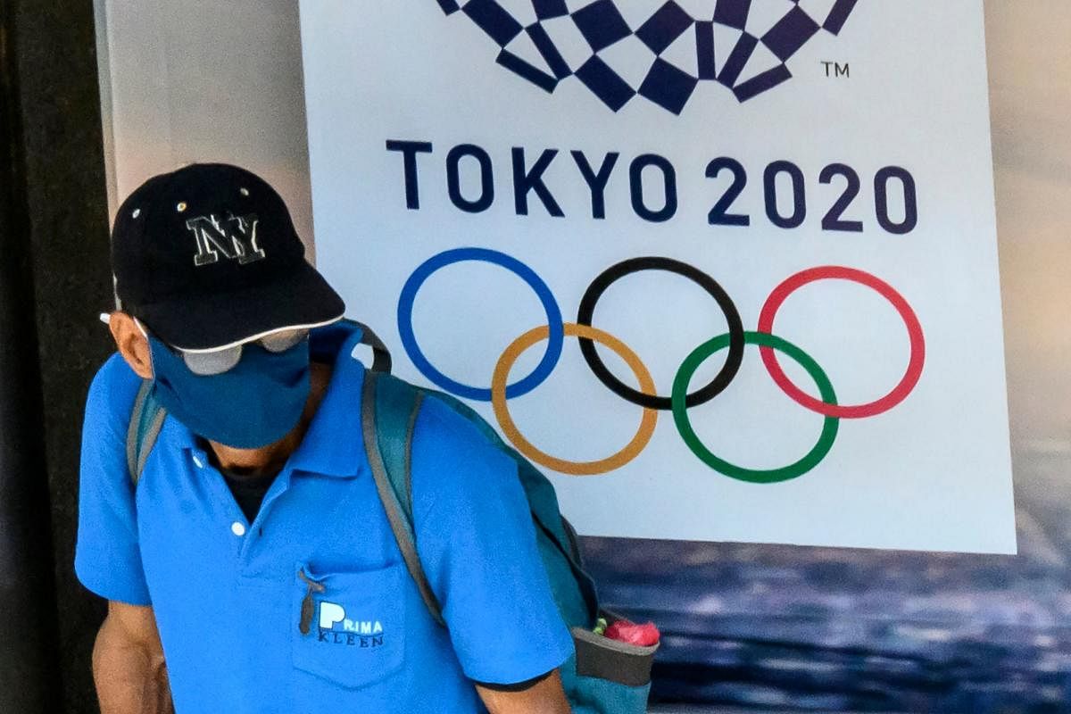 A man, wearing a face mask aas a preventive measure against the spread of the COVID-19 novel coronavirus, sits at a bus stop in front of an advertisement for the Tokyo 2020 Summer Olympics Games (AFP Photo)
