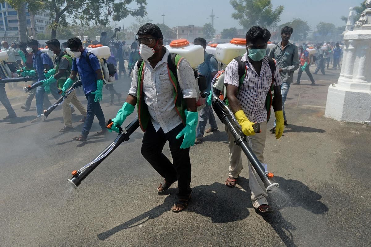 Health workers wearing facemasks amid concerns over the spread of the COVID-19 novel coronavirus, spray disinfectant at the corporation office in Chennai on March 20, 2020. (AFP Photo)
