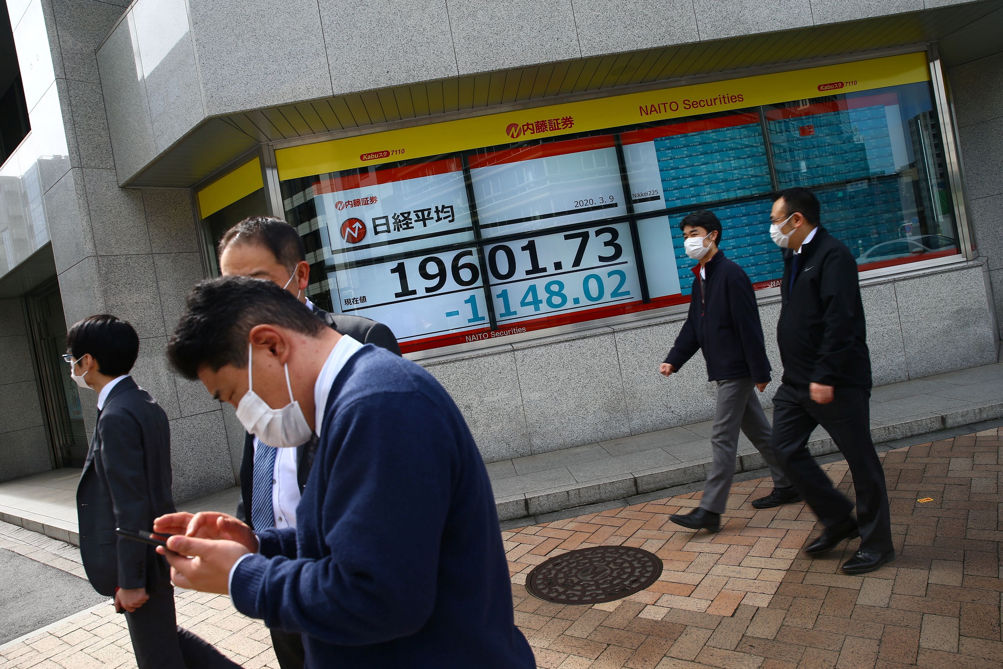 People wearing protective face masks are seen near an electronic display showing the Nikkei index (Reuters file photo)