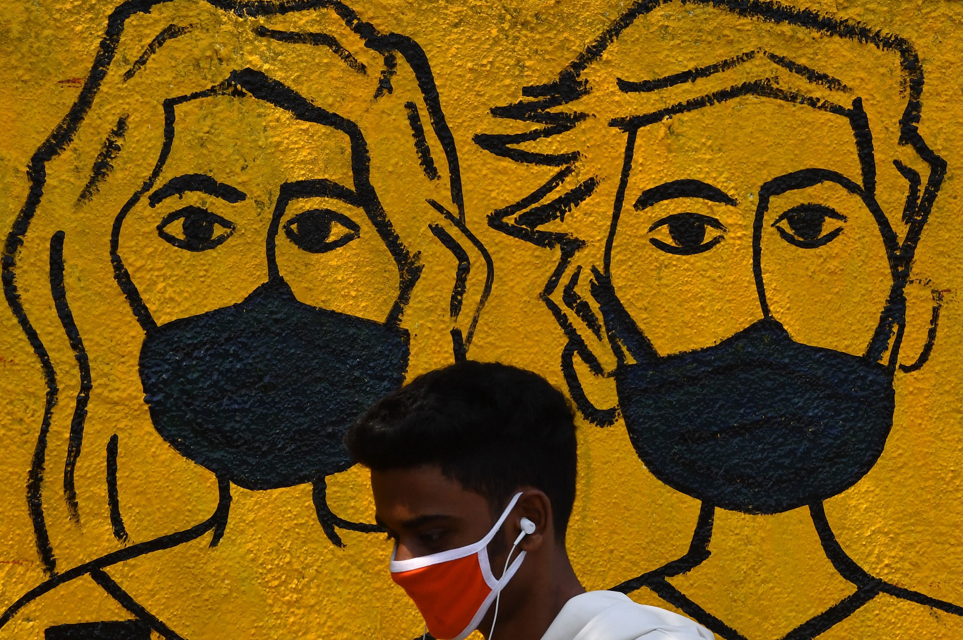 A youth wearing a facemask walk past a mural depicting people wearing famcemaks during the first day of a 21-day government-imposed nationwide lockdown as a preventive measure against the COVID-19 coronavirus, in Mumbai. (Credit: AFP)