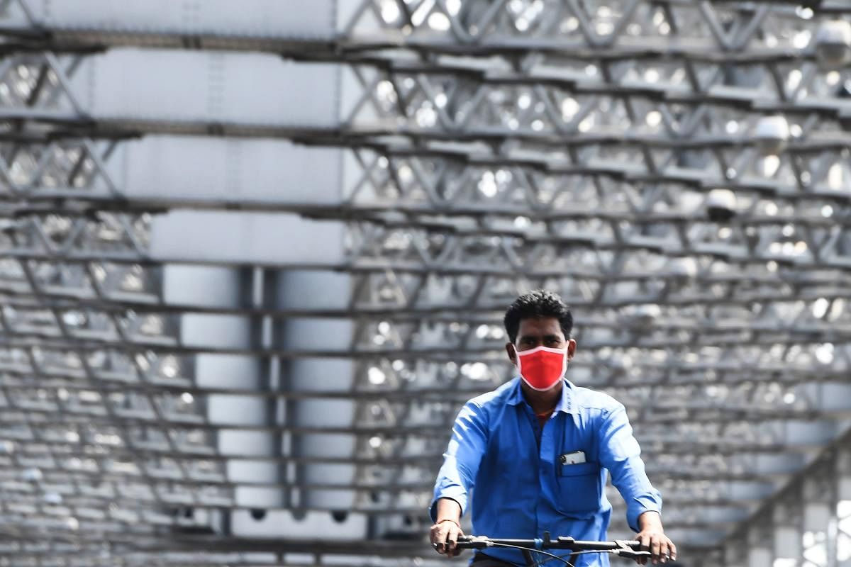 A man wearing a facemaks rides a bike across the Howrah Bridge during a one-day Janata (civil) curfew imposed amid concerns over the spread of the COVID-19 novel coronavirus, in Kolkata on March 22, 2020. Credit: AFP Photo