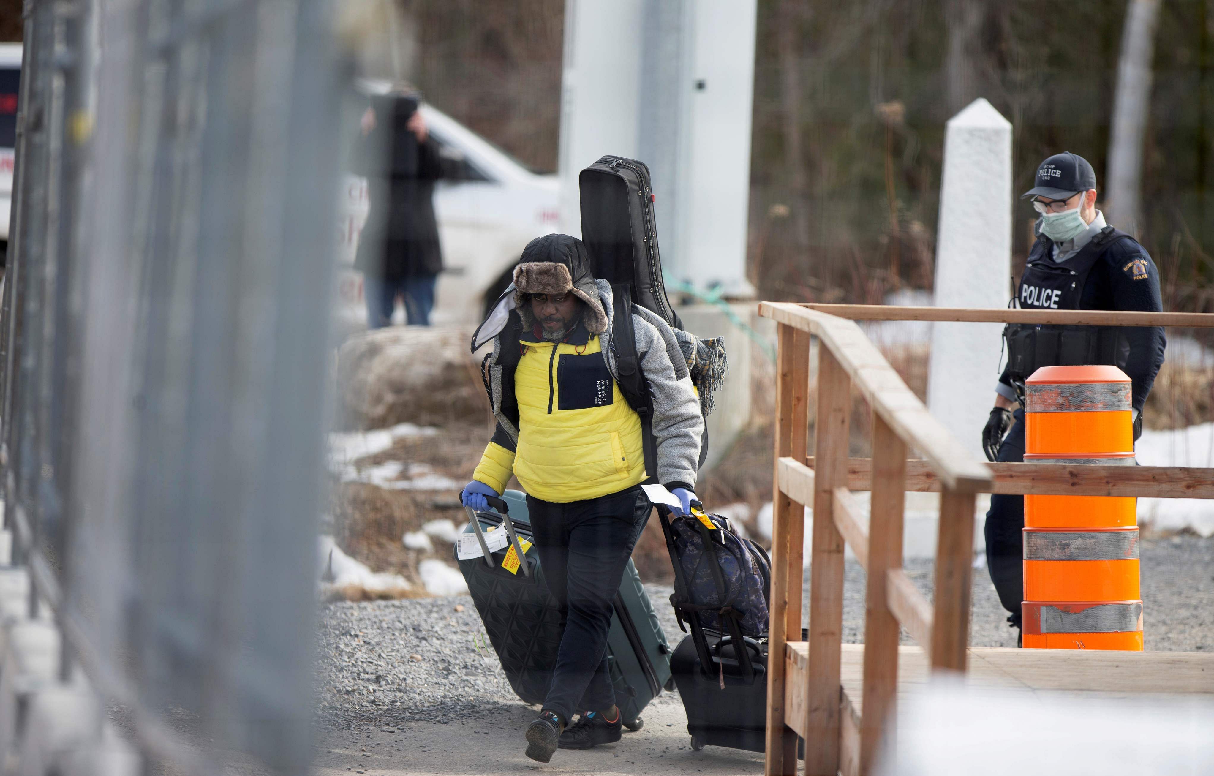 FILE PHOTO: An asylum seeker crosses the border from New York into Canada followed by a Royal Canadian Mounted Police (RCMP) officer at Roxham Road in Hemmingford, Quebec, Canada. (Credit: Reuters)