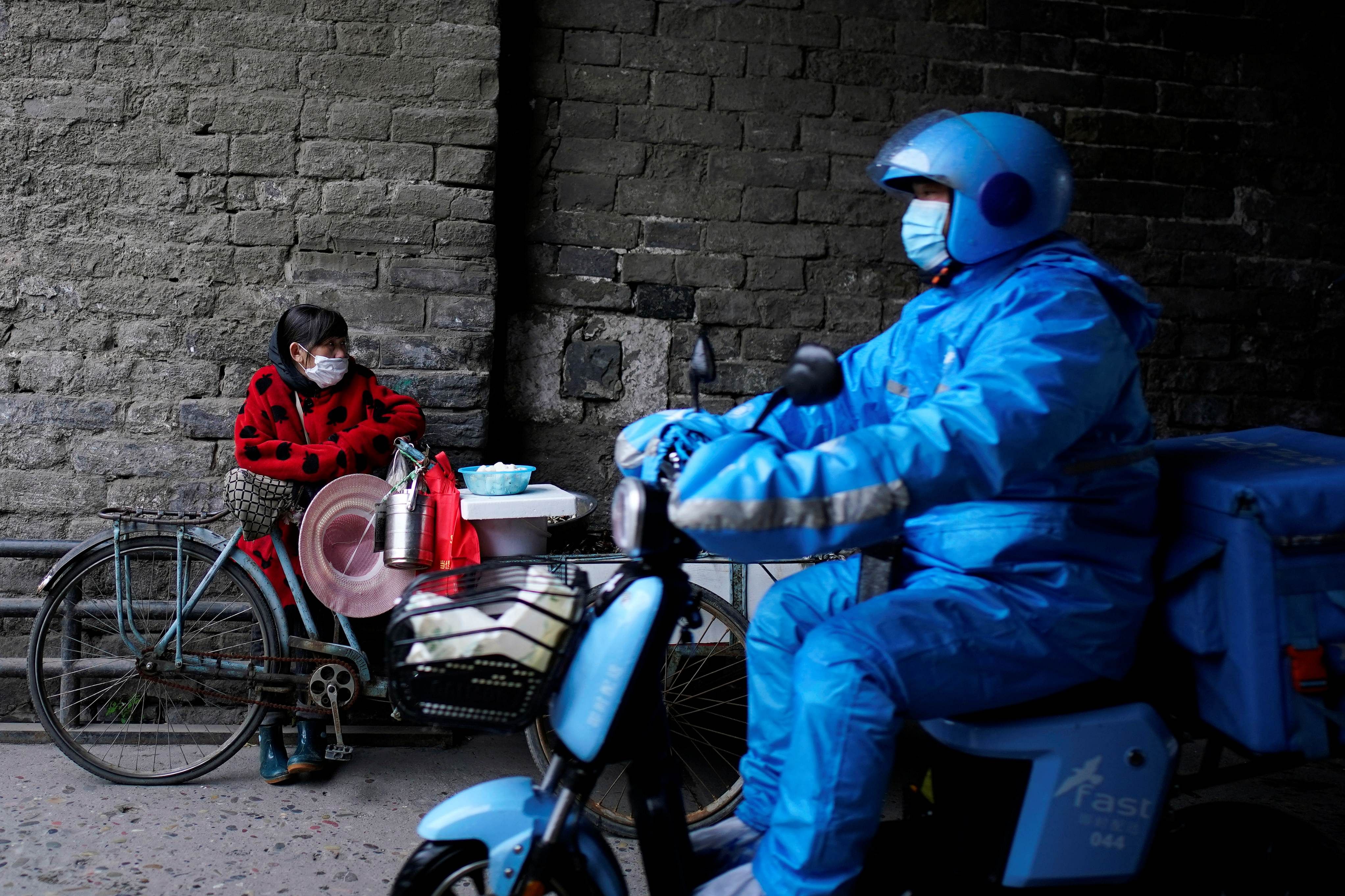 A delivery worker rides a vehicle past a vendor waiting for customers in Jingzhou, after the lockdown was eased in Hubei province. (Credit: Reuters)