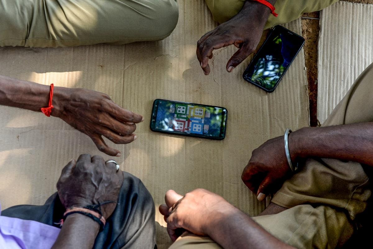Drivers play a game on a mobile phone as they wait for customers, due to national and international travel restrictions and concerns over the spread of the COVID-19 coronavirus, at the prepaid taxi stand at Chennai International Airport in Chennai on March 19, 2020. (Photo by Arun SANKAR / AFP)