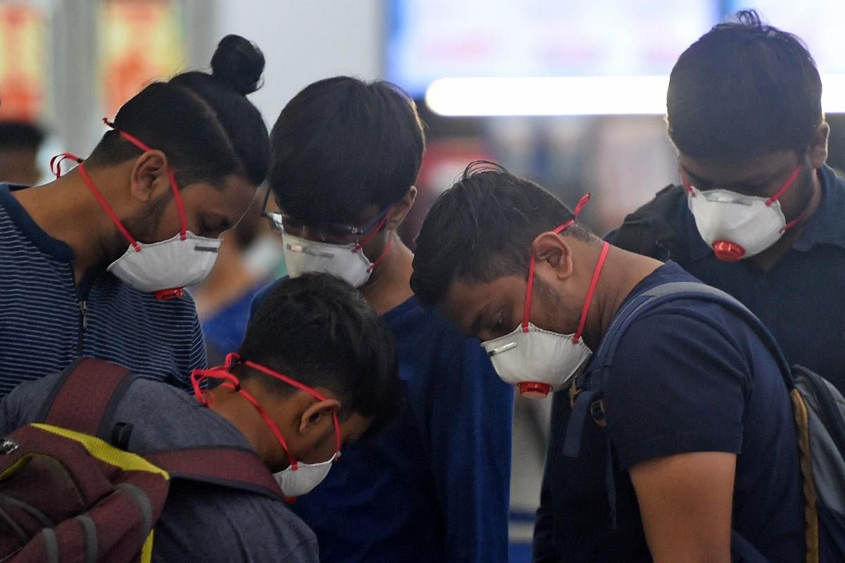 Passengers wearing facemasks amid concerns over the spread of the COVID-19 novel coronavirus, stand in a queue at a counter inside the airport in Goa on March 15, 2020. (Photo by Punit PARANJPE / AFP)