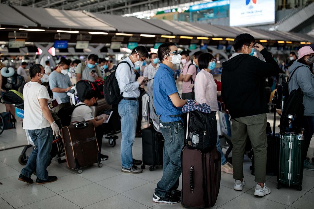 People wearing face masks wait in check-in lines as airlines cancelled dozens of flights amid concerns over the spread of the COVID-19 coronavirus at Suvarnabhumi Airport in Bangkok on March 25, 2020. Credit: AFP Photo