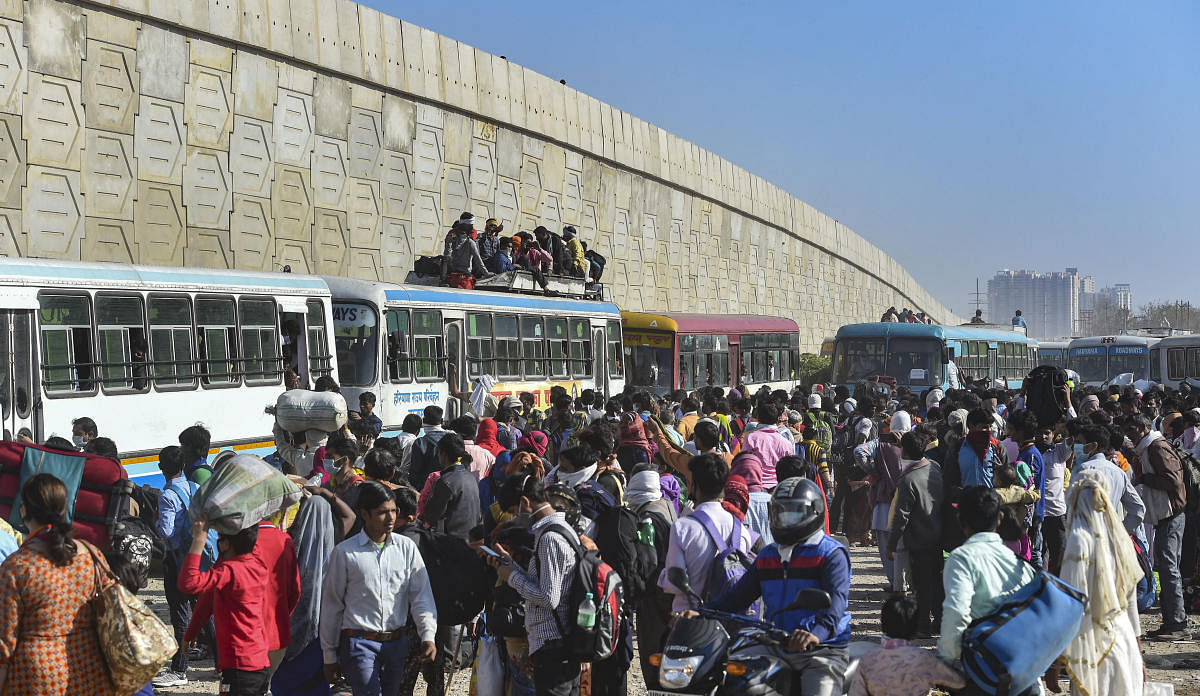 Migrant workers along with their family members wait to board buses to their respective villages, amid a nationwide lockdown in wake of coronavirus pandemic, at Lal Quarter Bus Stand in New Delhi. (PTI Photo)