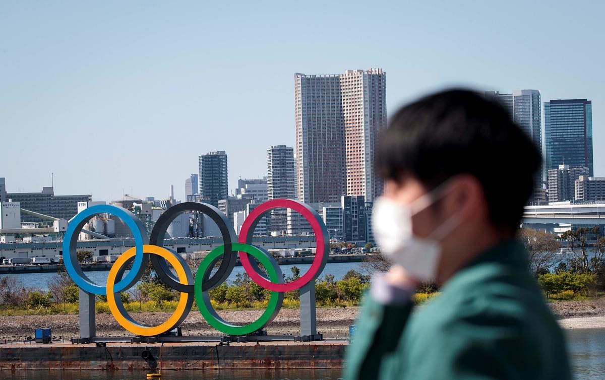 A man wearing a face mask, amid concerns over the spread of the COVID-19 novel coronavirus, stands before the Olympic rings (AFP Photo)