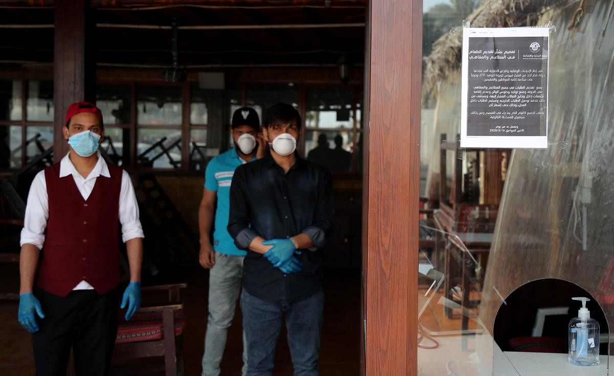 Mask-clad workers stand inside a closed-down cafe in Qatar's capital Doha (AFP Photo)