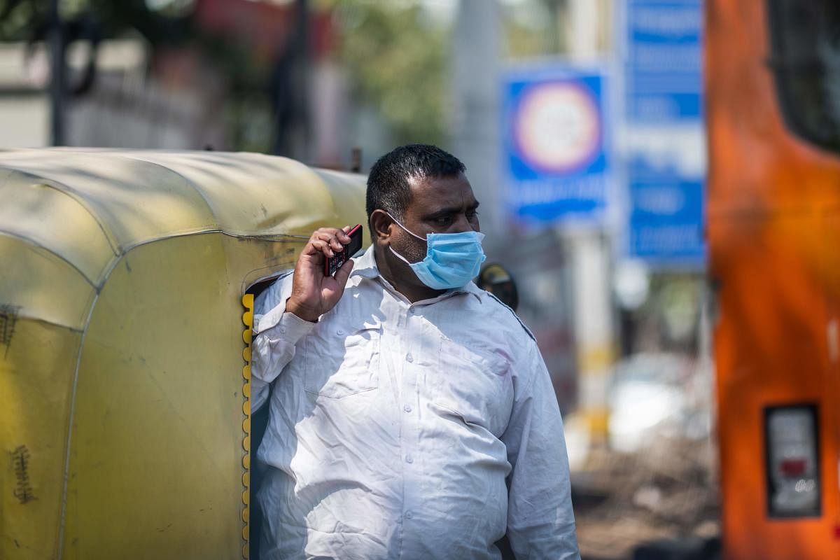 An auto-rickshaw driver wearing a facemask as a preventive measure against the COVID-19 coronavirus speaks on his mobile phone as he waits for passengers in New Delhi on March 18, 2020. (Photo by Jewel SAMAD / AFP)