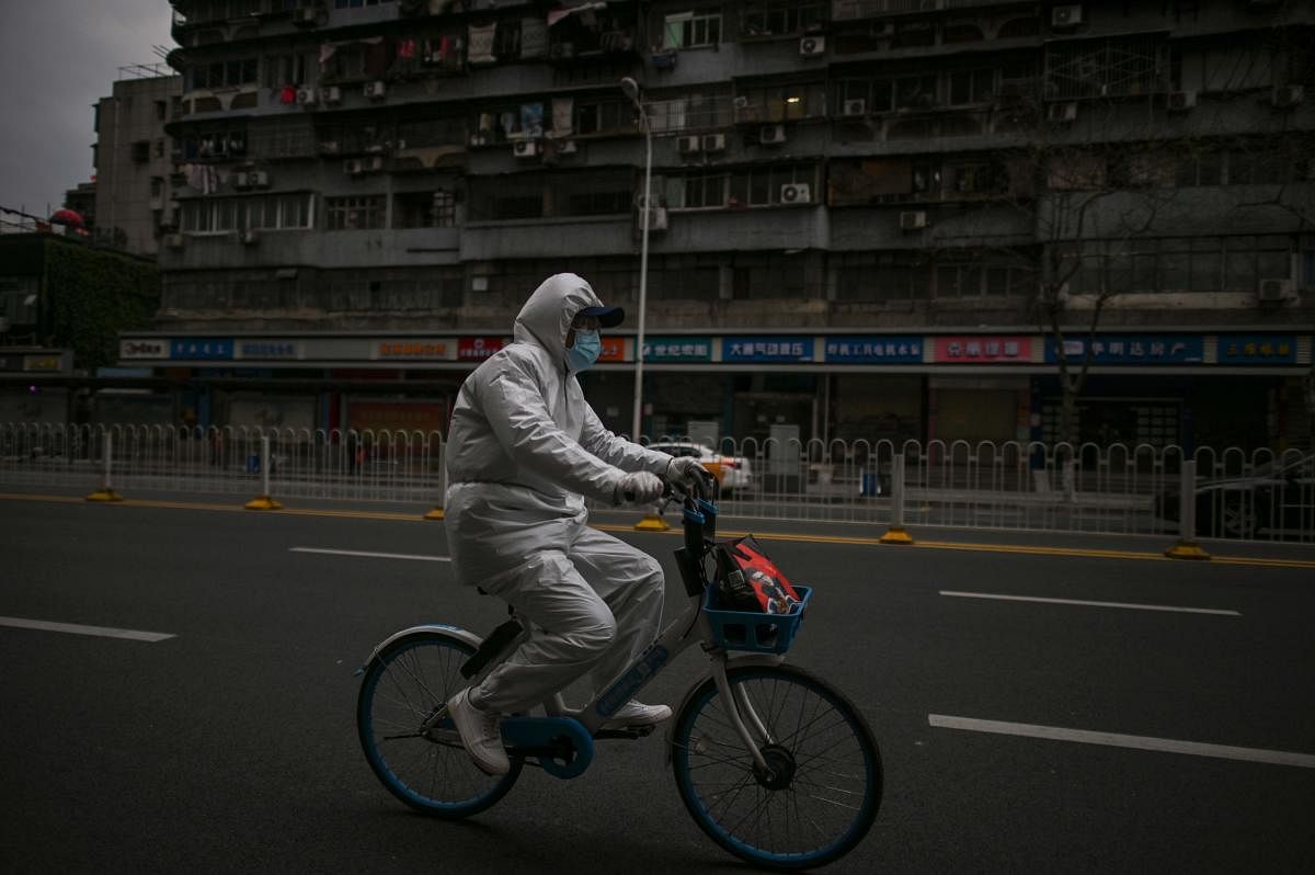  A man wearing a protective suit rides a bicycle on a street in Wuhan, in China's central Hubei province, on April 1, 2020, where the COVID-19 coronavirus first emerged last year but is partly reopening after more than two months of near total isolation. (Photo by HECTOR RETAMAL / AFP)