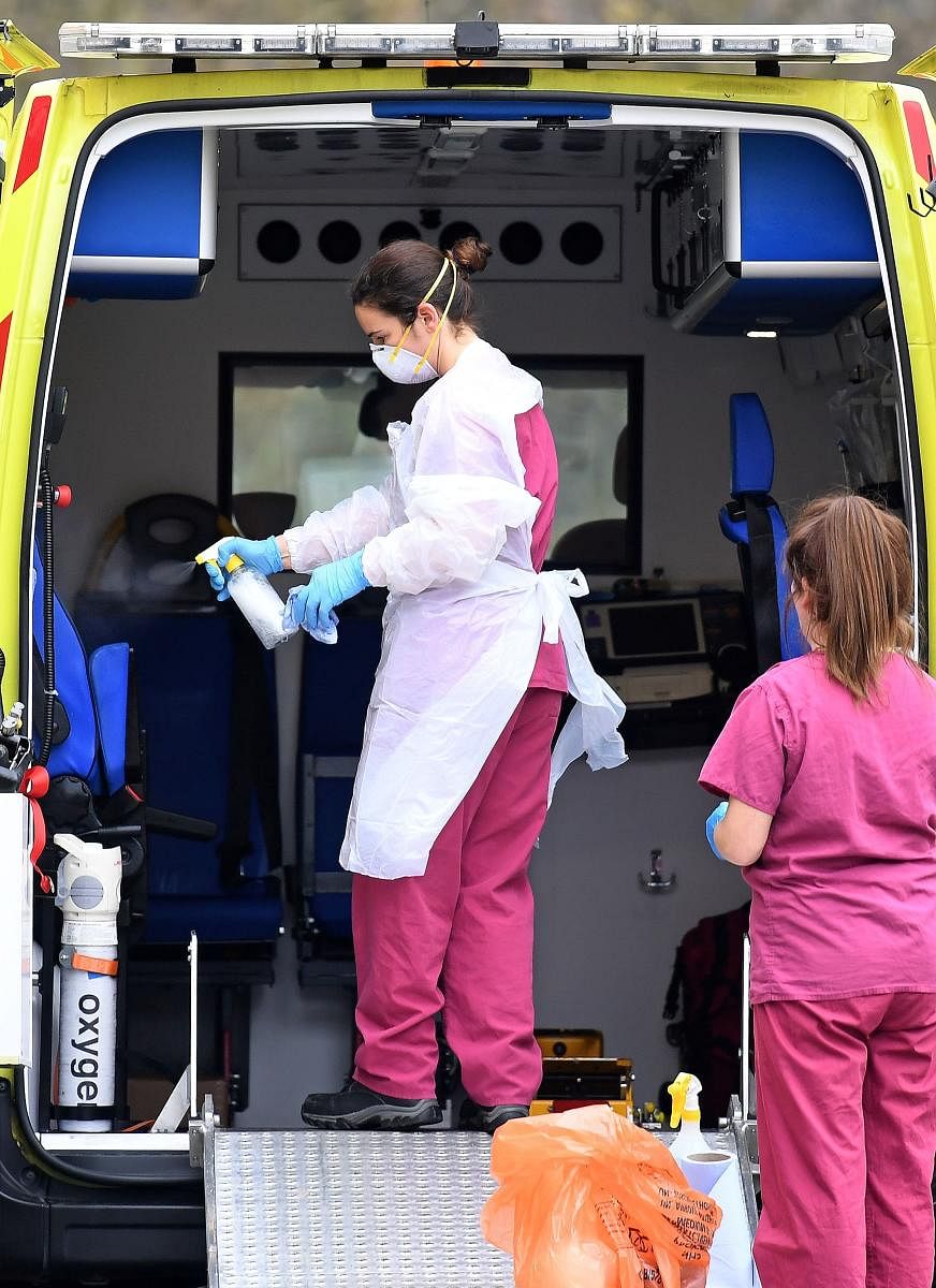A member of medical staff wearing PPE of gloves, an apron and a face mask as a preactionary measure against COVID-19, disinfects an ambulance. AFP