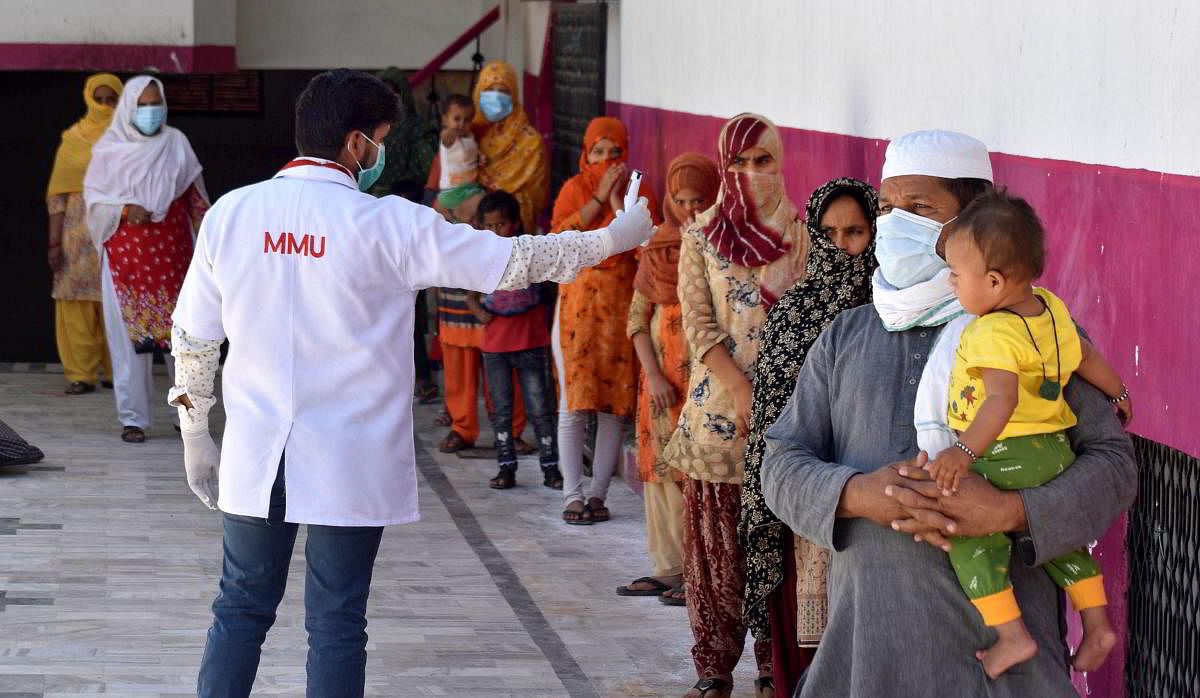 A medics checks the temperature of attendees of a religious congregation in Delhi's Nizamuddin area during their isolation period at a COVID 19 quarantine facility in Prayagraj. Credit: PTI Photo