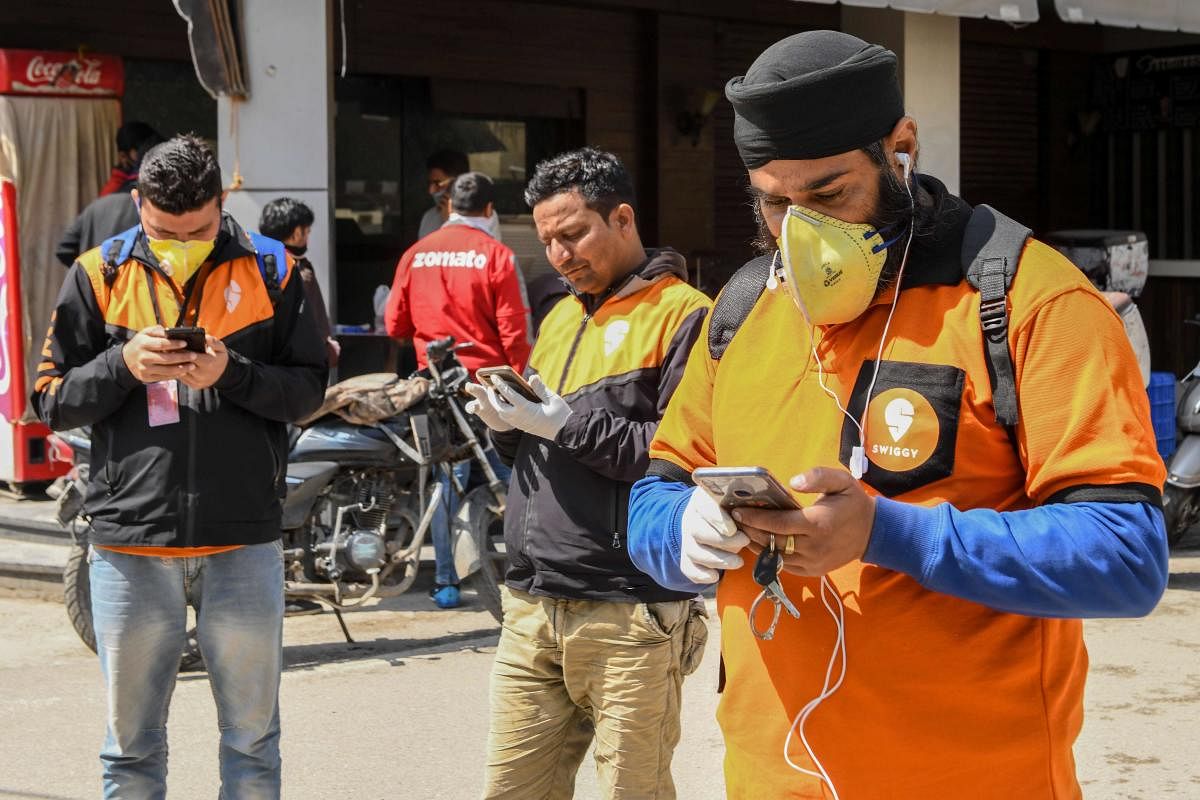 Swiggy delivery men check their mobile phones to deliver food commodities during a government-imposed nationwide lockdown as a preventive measure against the COVID-19 coronavirus, in Amritsar on March 28, 2020. Credit: AFP Photo