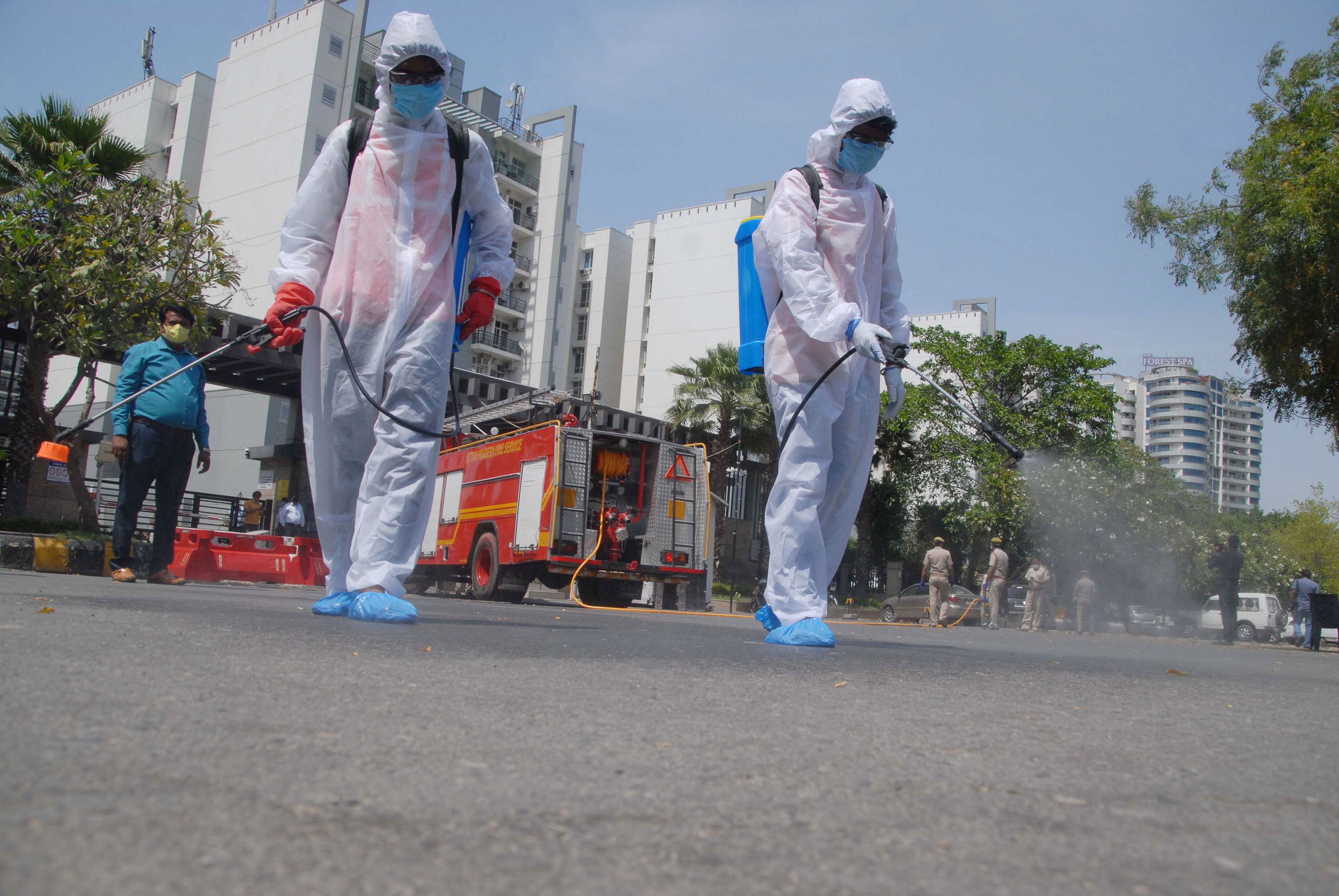Volunteers wearing protective suits sprays disinfectant outside a housing society, to curb the spread of coronavirus, during the nationwide lockdown, in Noida. (Credit: PTI)
