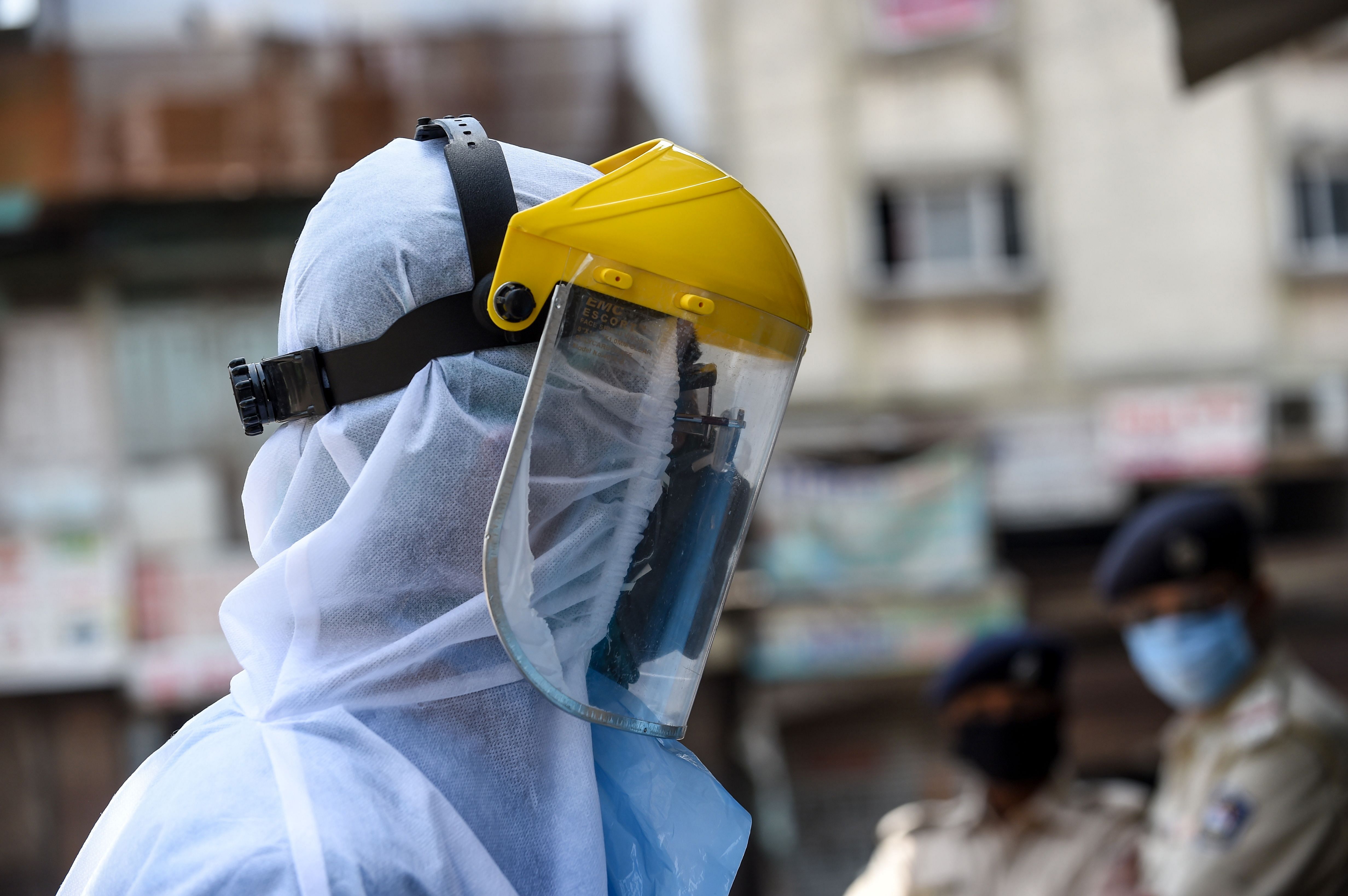 A health worker wearing protective gear walks past police personnel (background) during a screening and checking session at a residential area during a government-imposed nationwide lockdown as a preventive measure against the COVID-19 coronavirus, in Ahmedabad. (AFP Photo)