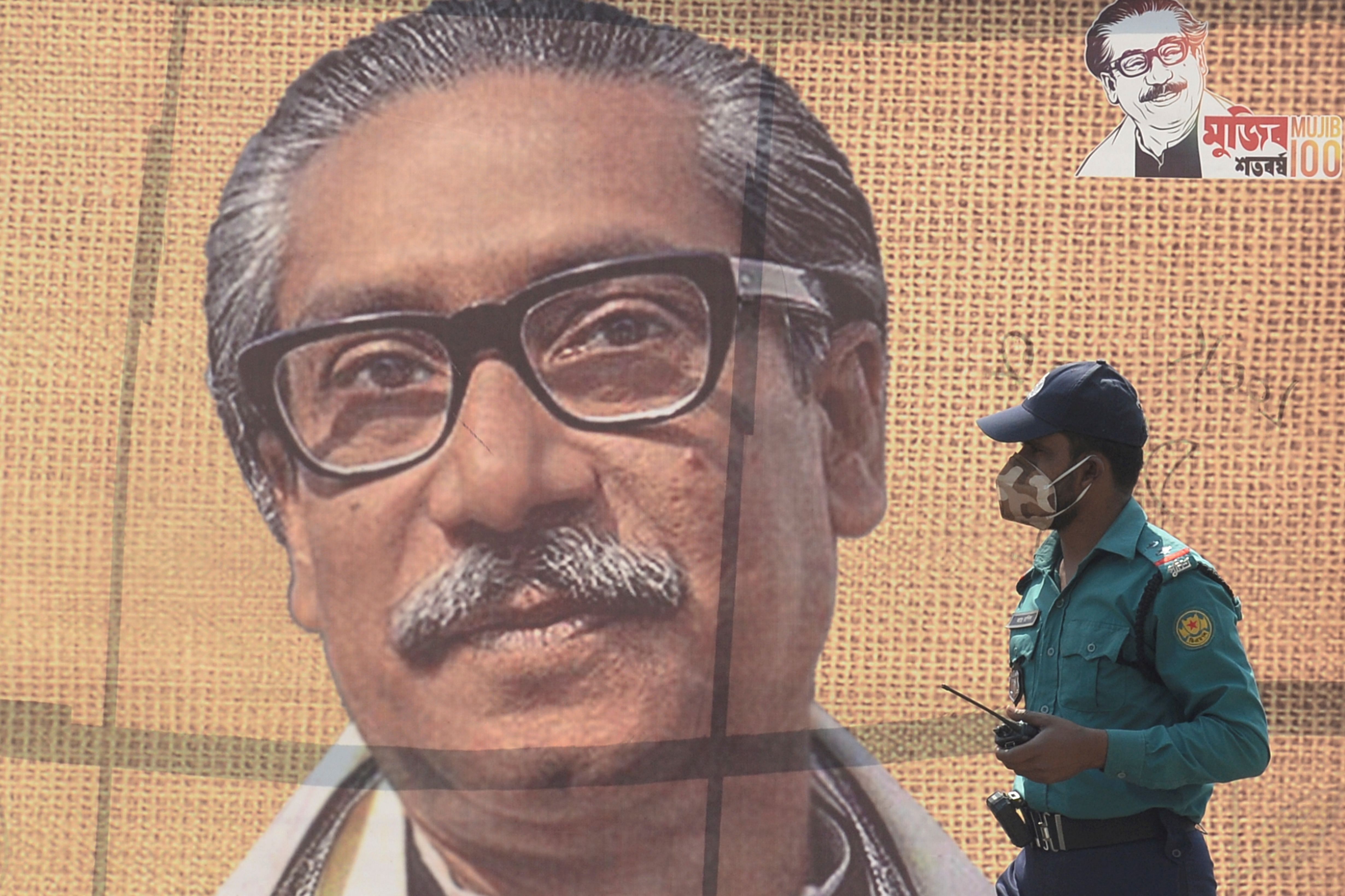 A policeman wearing a facemask amid fears of the spread of COVID-19 novel coronavirus, walks past a banner with a picture of Bangladesh’s founder Sheikh Mujibur Rahman. (AFP Photo)