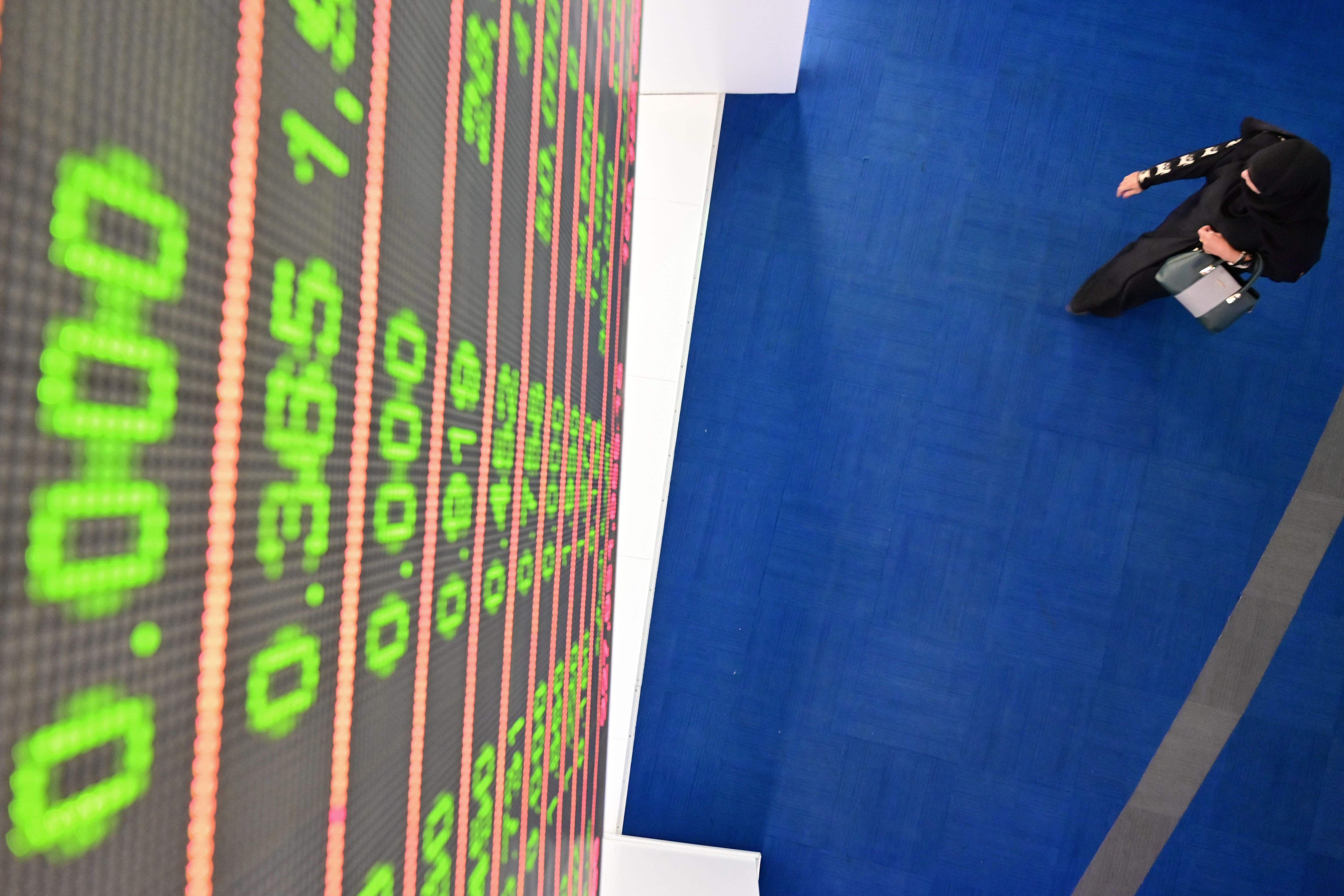 An Emirati woman walks underneath a digital board displaying stock data at the Dubai Stock. (AFP Photo)
