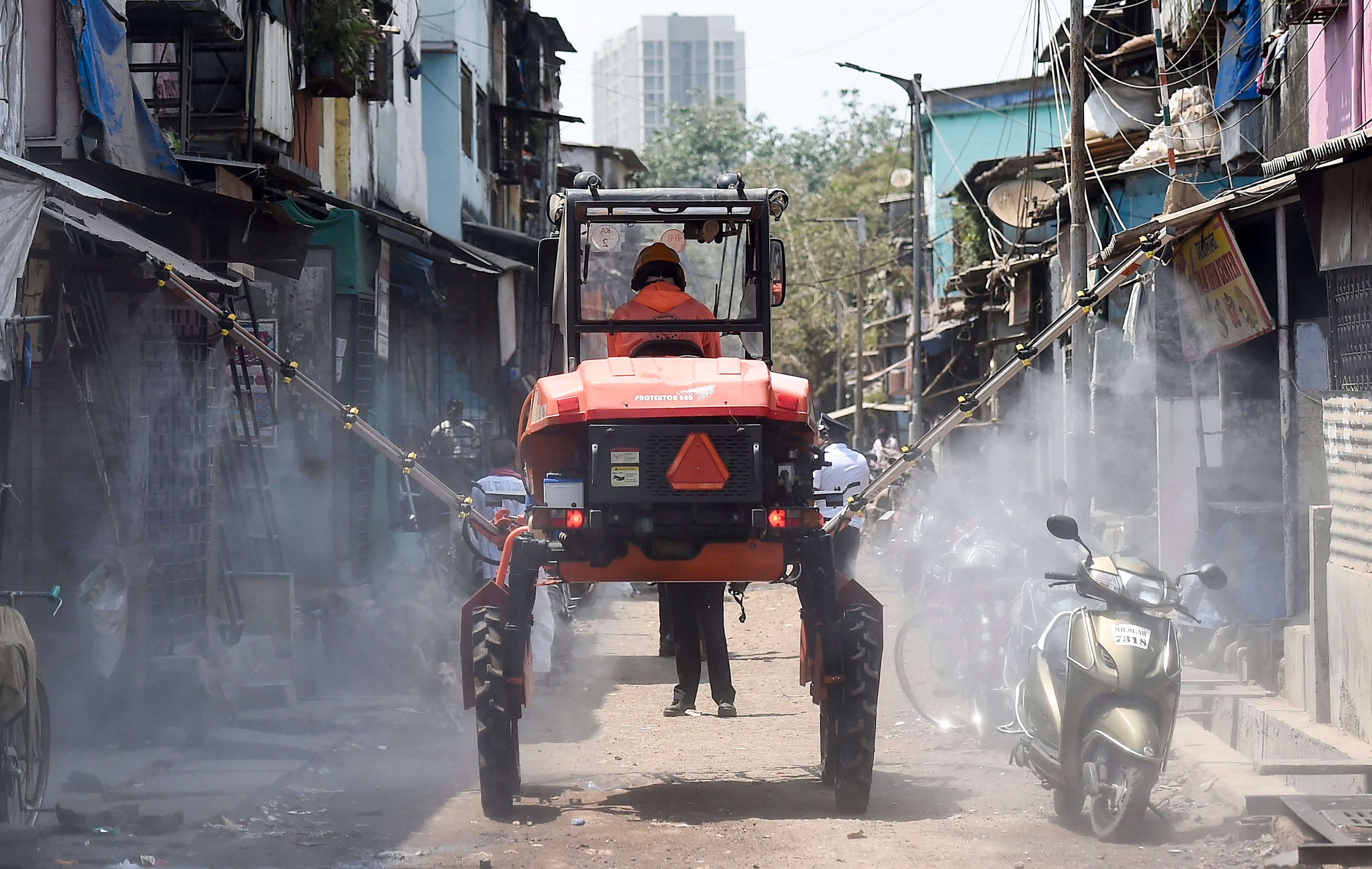 A firefighter decontaminates a road using a boom sprayer at Dharavi. (Credit: PTI)