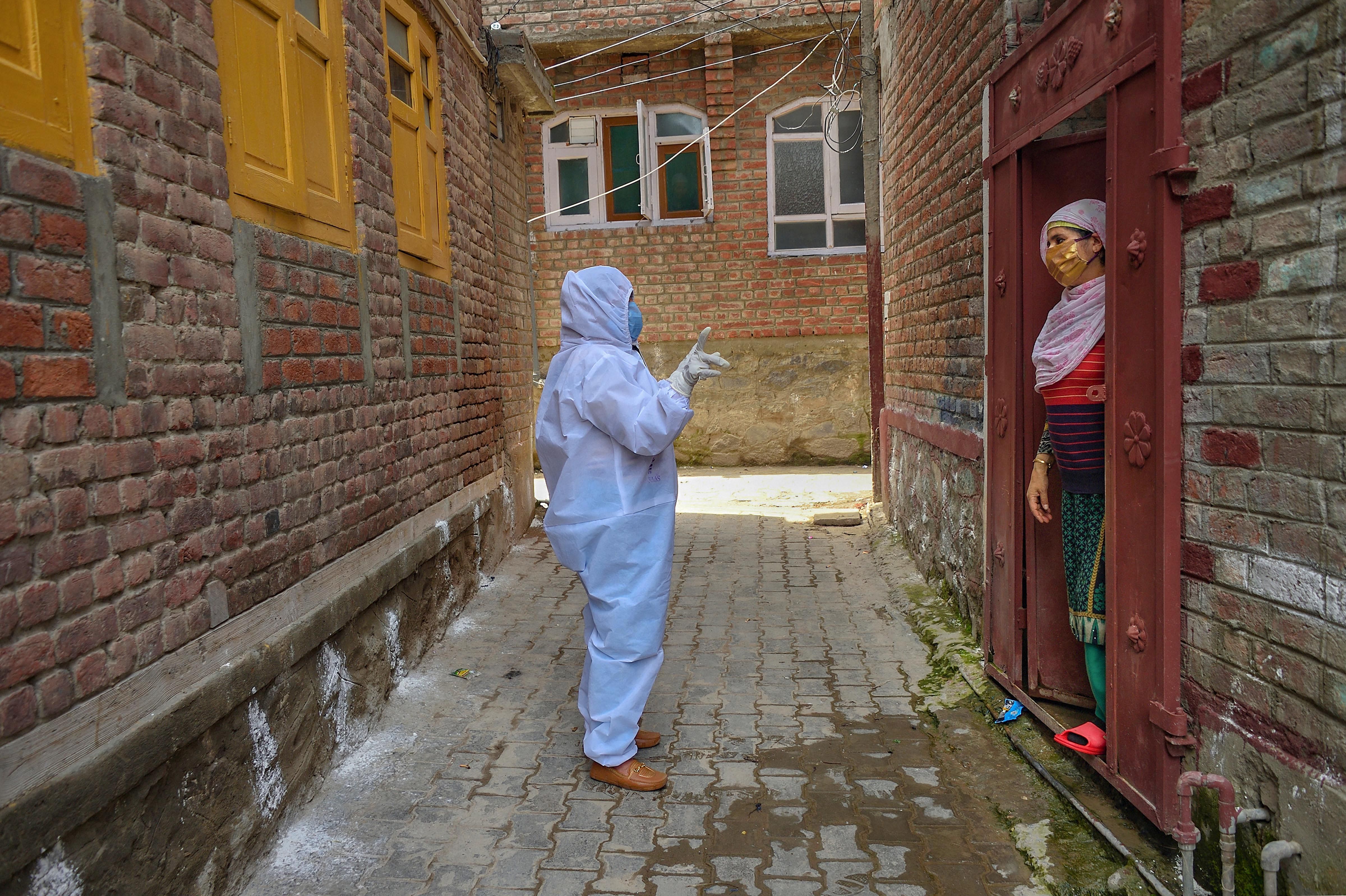 A health worker asks questions from a woman during a door-to-door surveillance in a red zone area for COVID-19. (Credit: PTI)