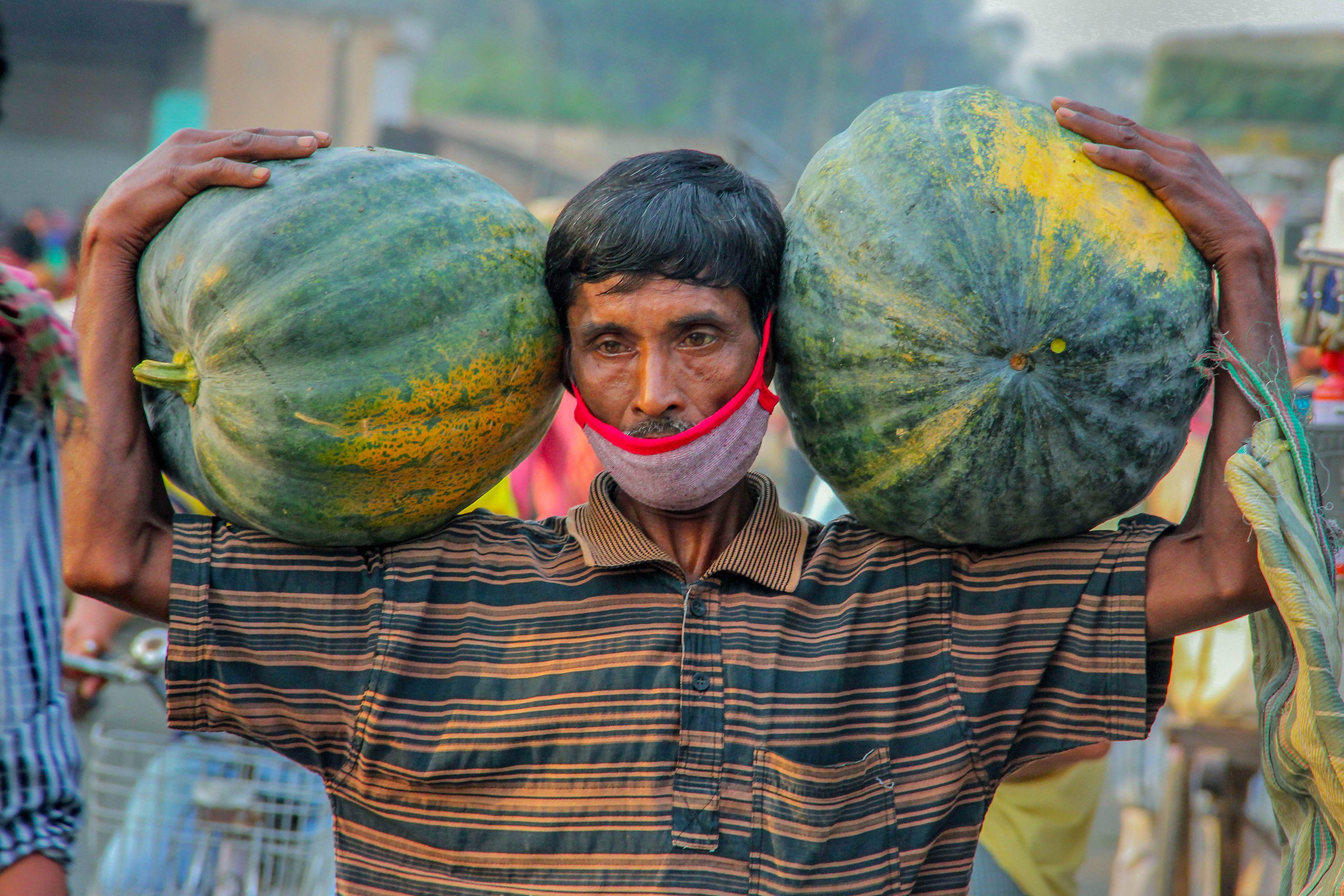 A farmer carries pumpkins on his shoulders at a market during the nationwide lockdown to curb the spread of coronavirus. (Credit: PTI Photo)