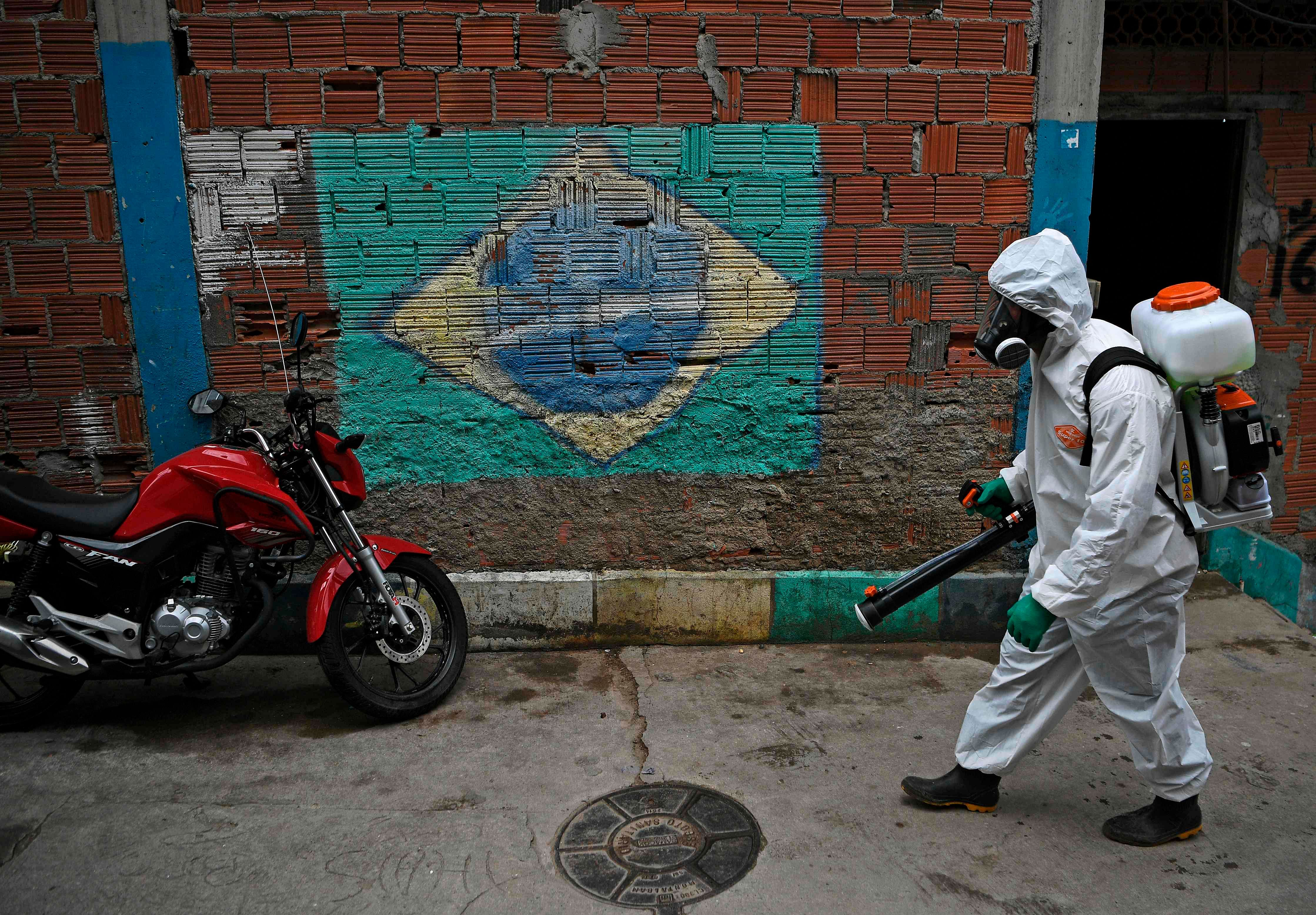 A volunteer walks past a mural of the Brazilian flag as he disinfects an area inside Babilonia favela, in Rio de Janeiro. (Credit: Reuters)