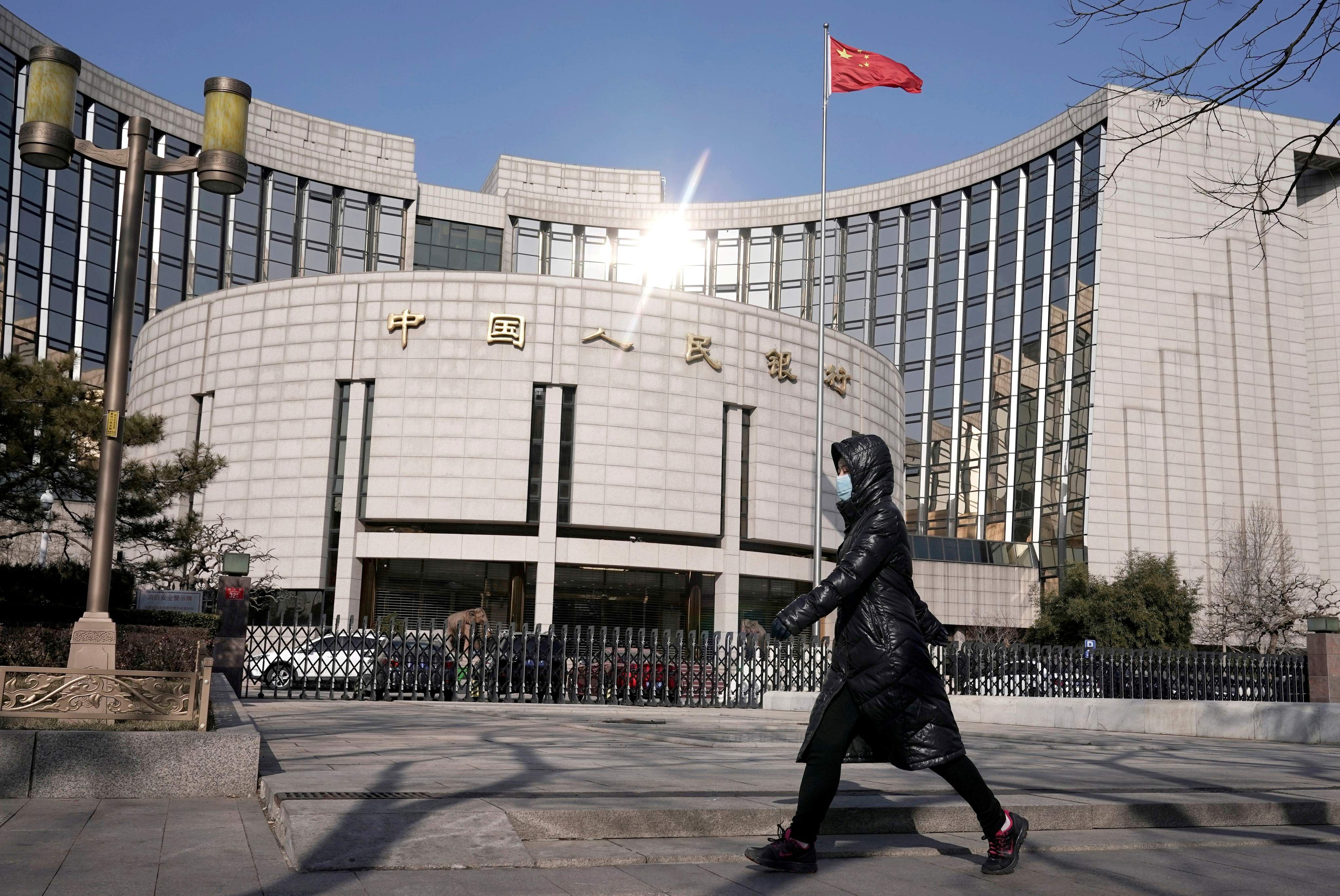  woman wearing a mask walks past the headquarters of the People's Bank of China. (Credit: Reuters)