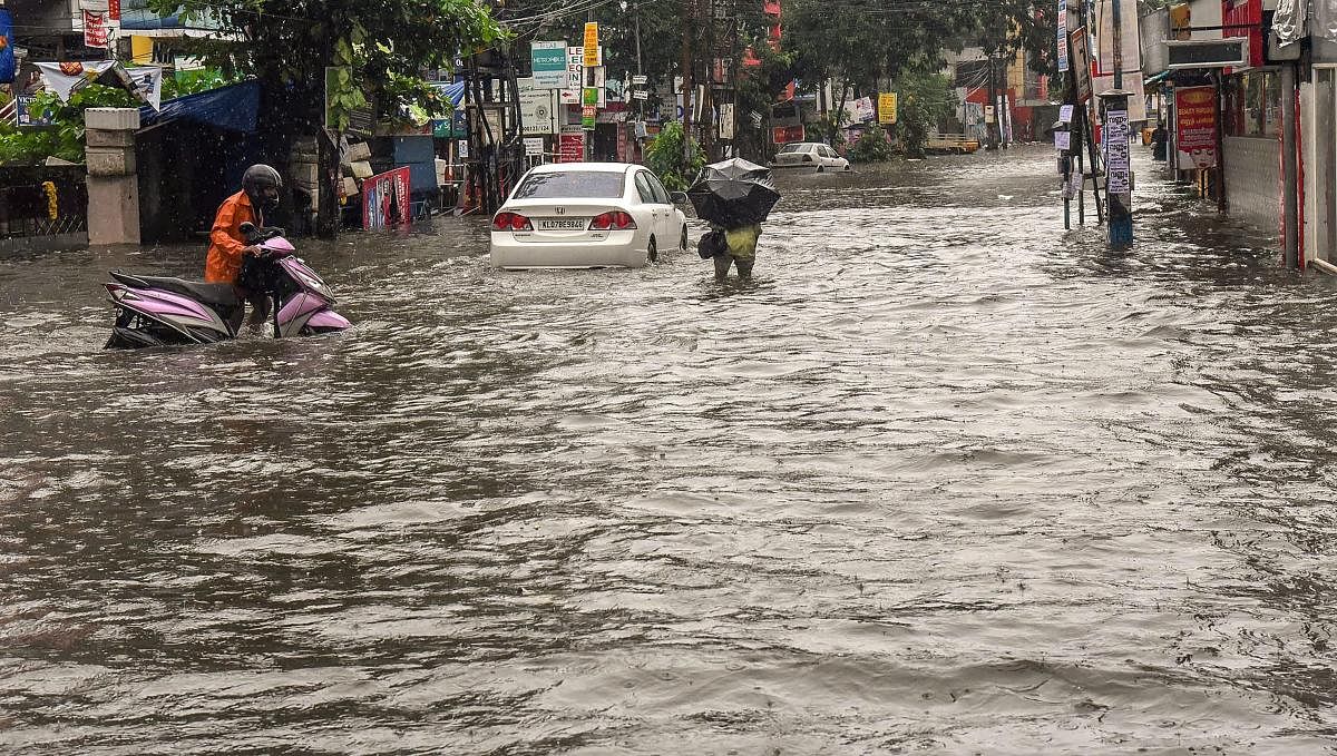 Commuters wade across a water-logged street surrounding the Ernakulam city after monsoon rainfall, in Kochi on Monday, July 16, 2018. (PTI Photo)