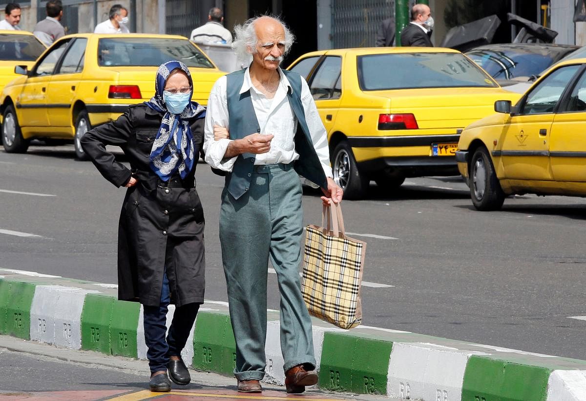 An elderly man and a woman, wearing a protective mask, walk along a street in Iran's capital Tehran. AFP