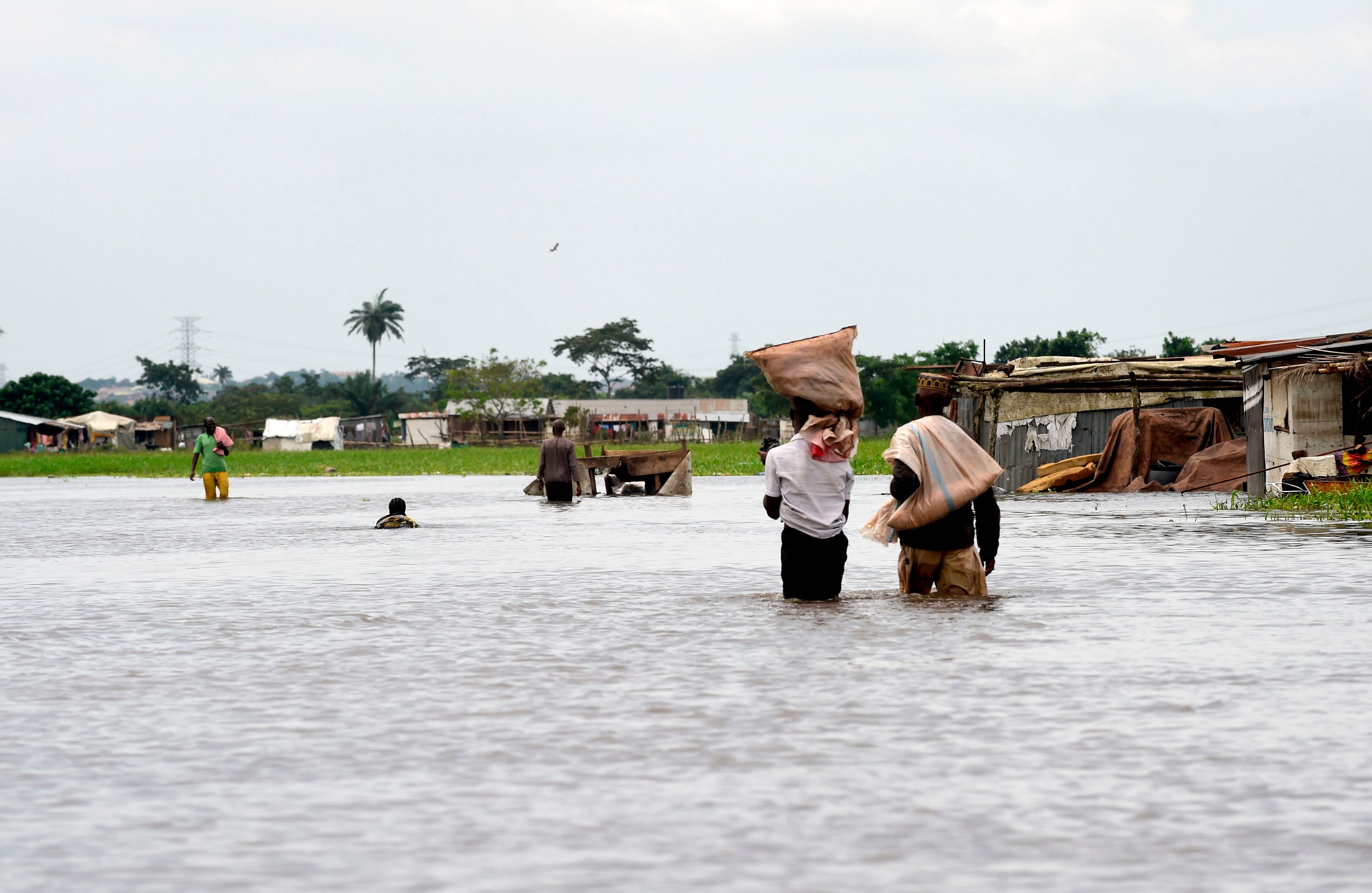 eople carry their belonging on their heads while they walk on a flooded road following heavy rain downpour in Wawa in Ogun State southwest Nigeria. (AFP Photo)