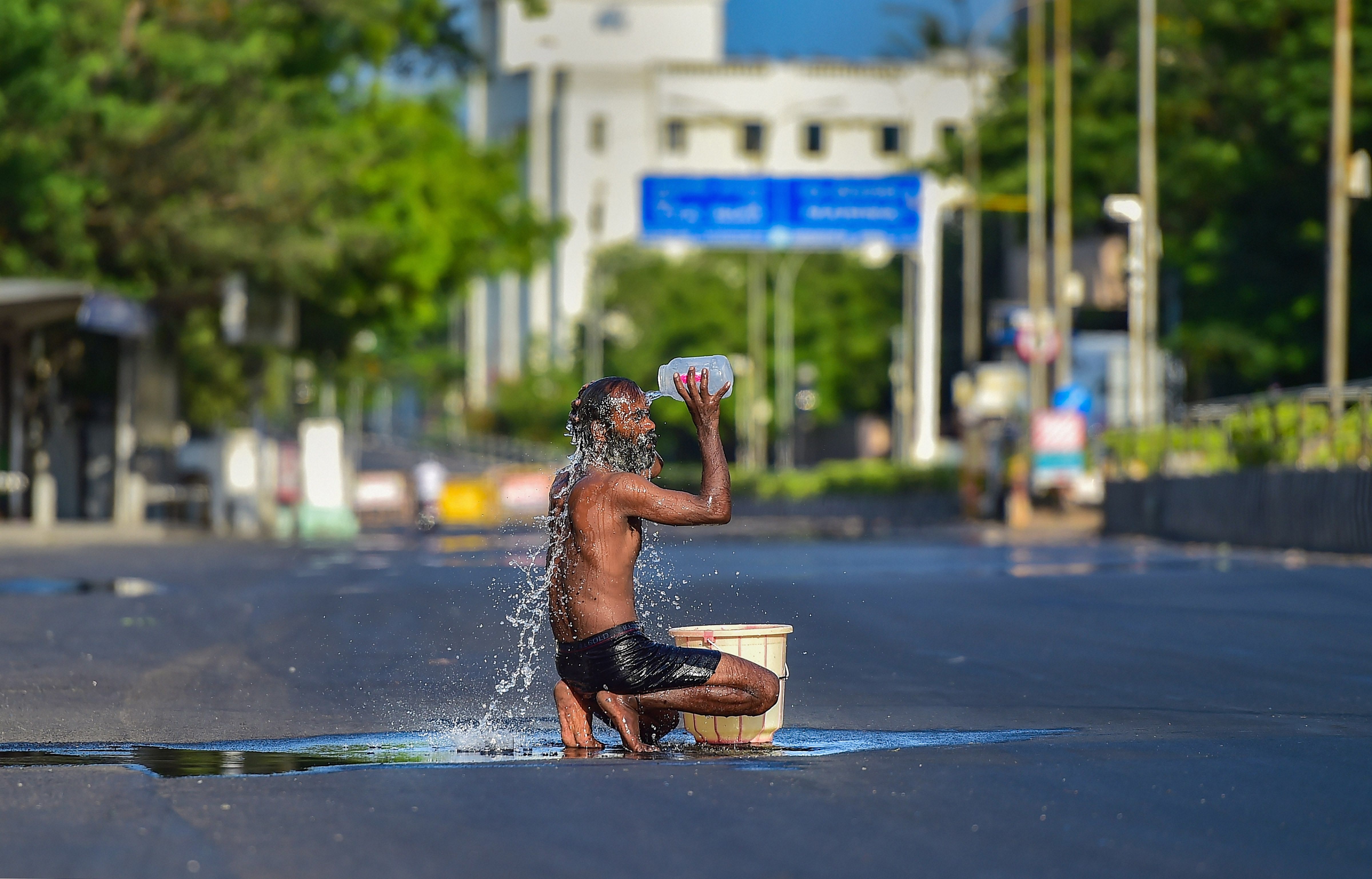  A man bathes on a deserted road after procuring water from a leaky pipeline, during a government-imposed nationwide lockdown. (Credit: PTI Photo)